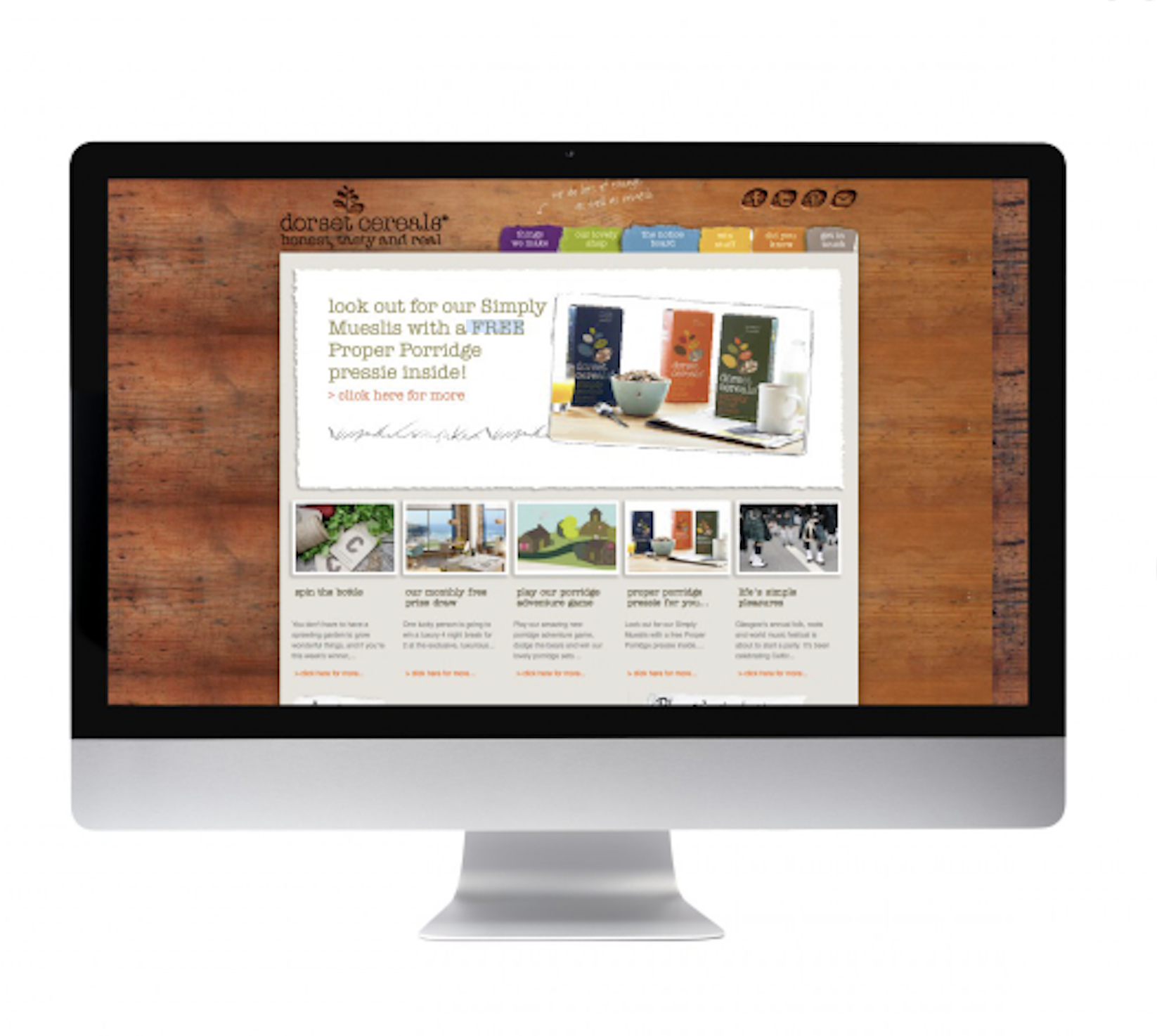A computer monitor displaying a website with a wooden background theme for a health food brand, featuring images of cereal products and promotional offers.