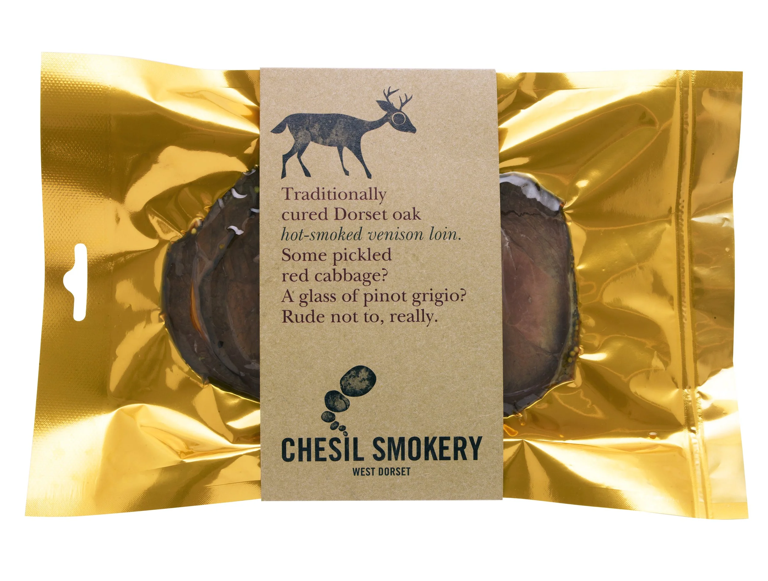 Packaged smoked venison loin with gold-colored wrapping and a beige label featuring a deer logo and description texts about Dorset oak smoked venison, produced by Chesil Smokery in West Dorset.