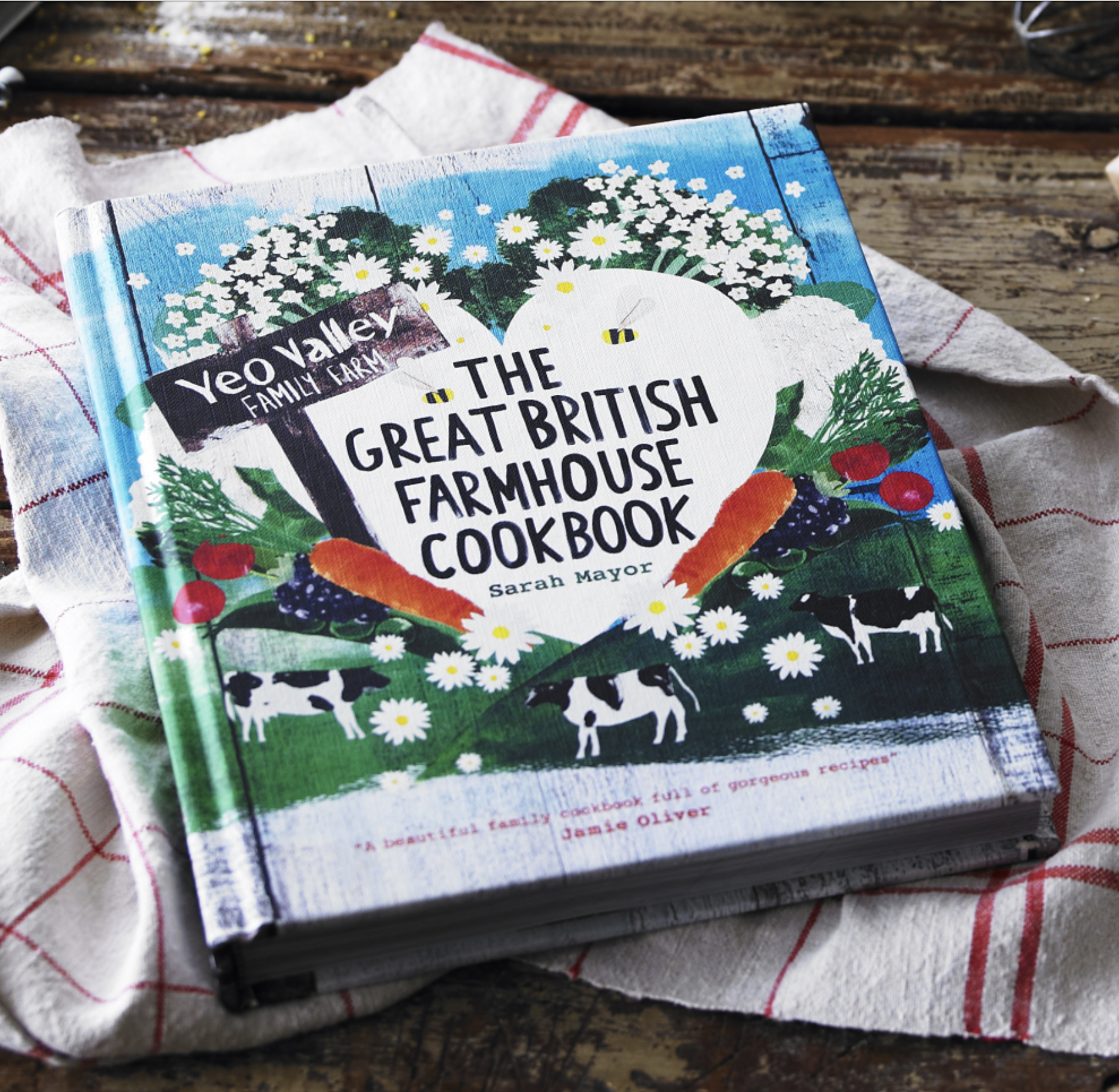 Cover of a book titled "The Great British Farmhouse Cookbook" on a rustic wooden table with a red and white checkered cloth.