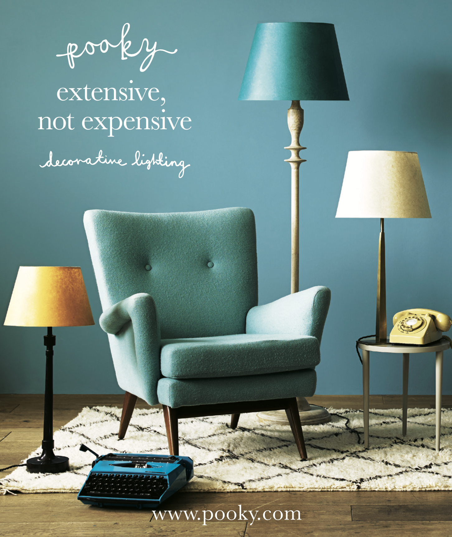 A vintage blue armchair on a black and white rug with a blue typewriter in front, a yellow rotary phone on a side table, and three standing lamps of different sizes and colors against a teal wall with white handwritten text about decorative lighting 