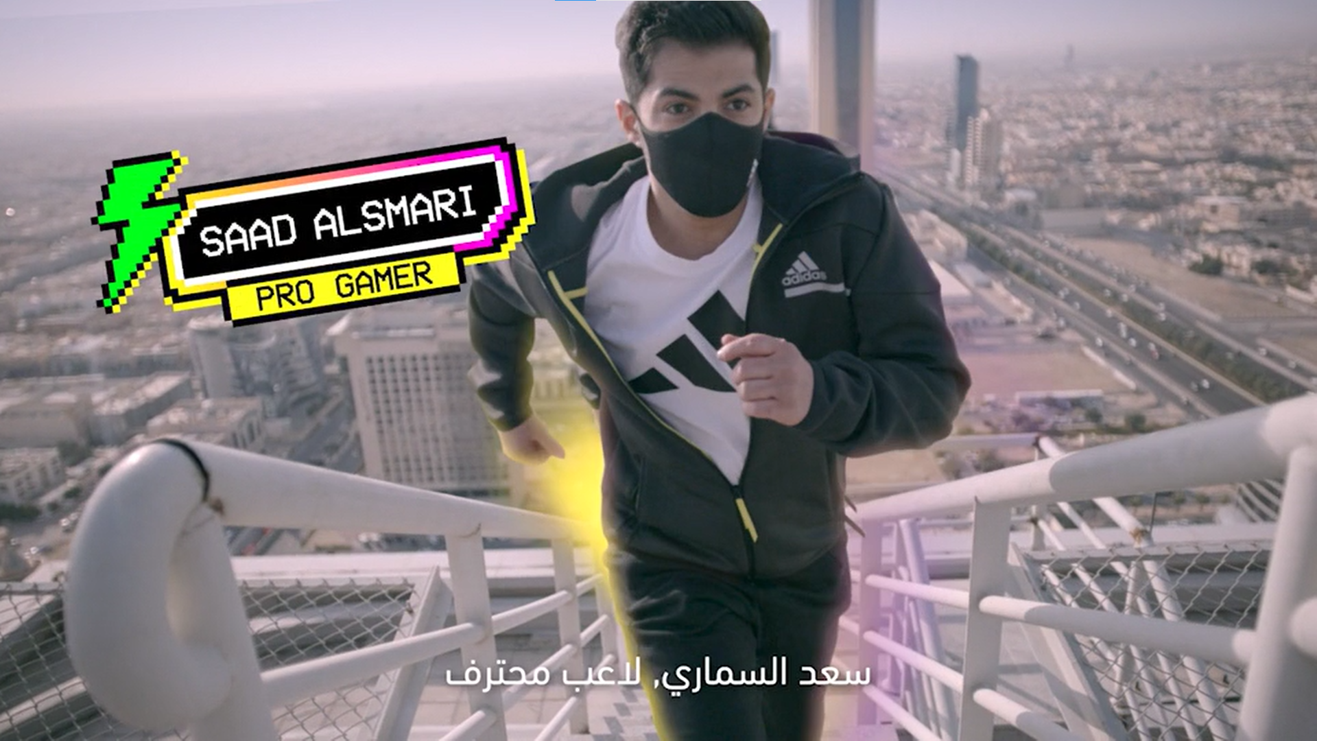 A young man wearing a black face mask, white t-shirt, and black jacket with yellow accents is running up a tall building's exterior on a staircase. The cityscape and tall buildings are visible in the background. The image has a graphic overlay with a