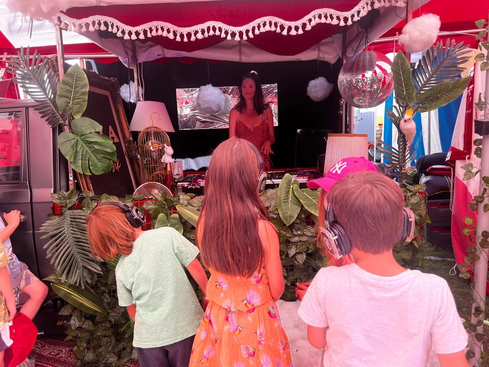 DJ auf einer Bühne mit Jungle-Dekor, Kinder beim Tanzen, umgeben von Pflanzen, Discokugel, Lampen und Dekorationen