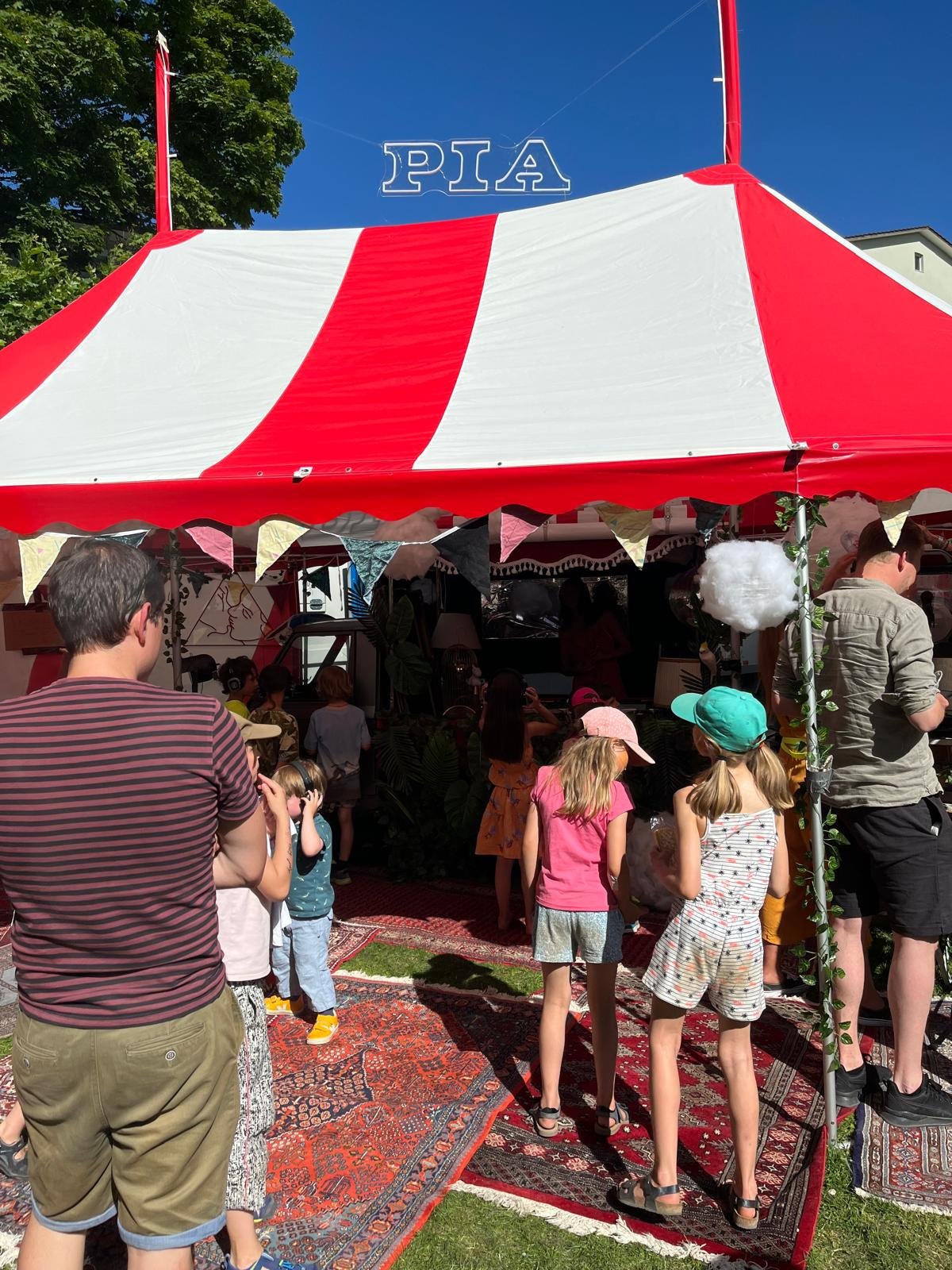 Kinder und Erwachsene stehen vor einem roten und weißen Zirkuszelt mit einem 