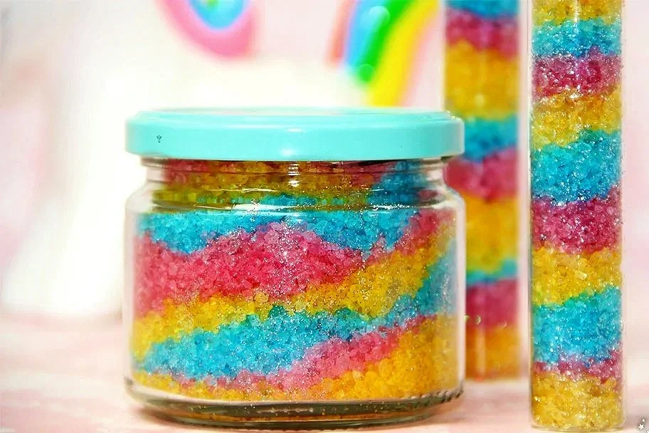 Bunte Zuckerstreusel in einem Glas mit blauem Deckel, weitere Streusel in einem Behälter im Hintergrund.