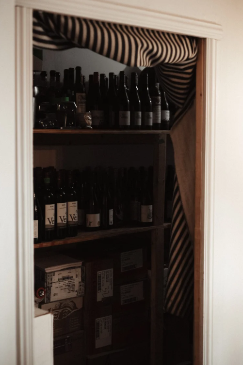 A small closet or storage space filled with wine bottles on shelves, with a striped fabric or curtain draped overhead.