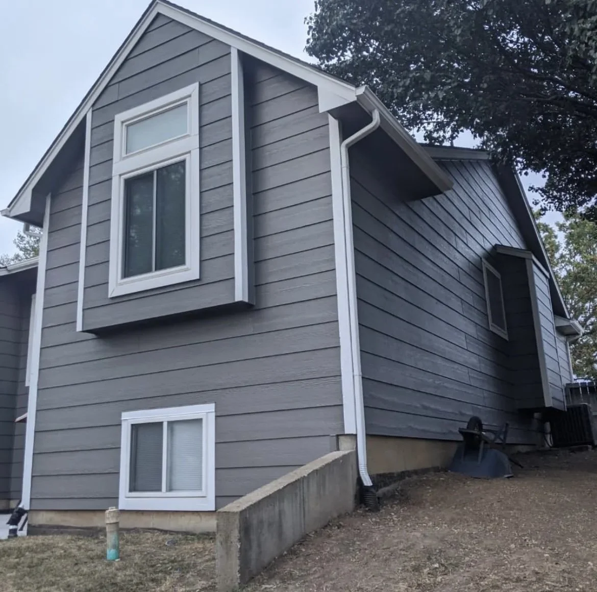 Grey house with white trim and two windows on a sloped yard