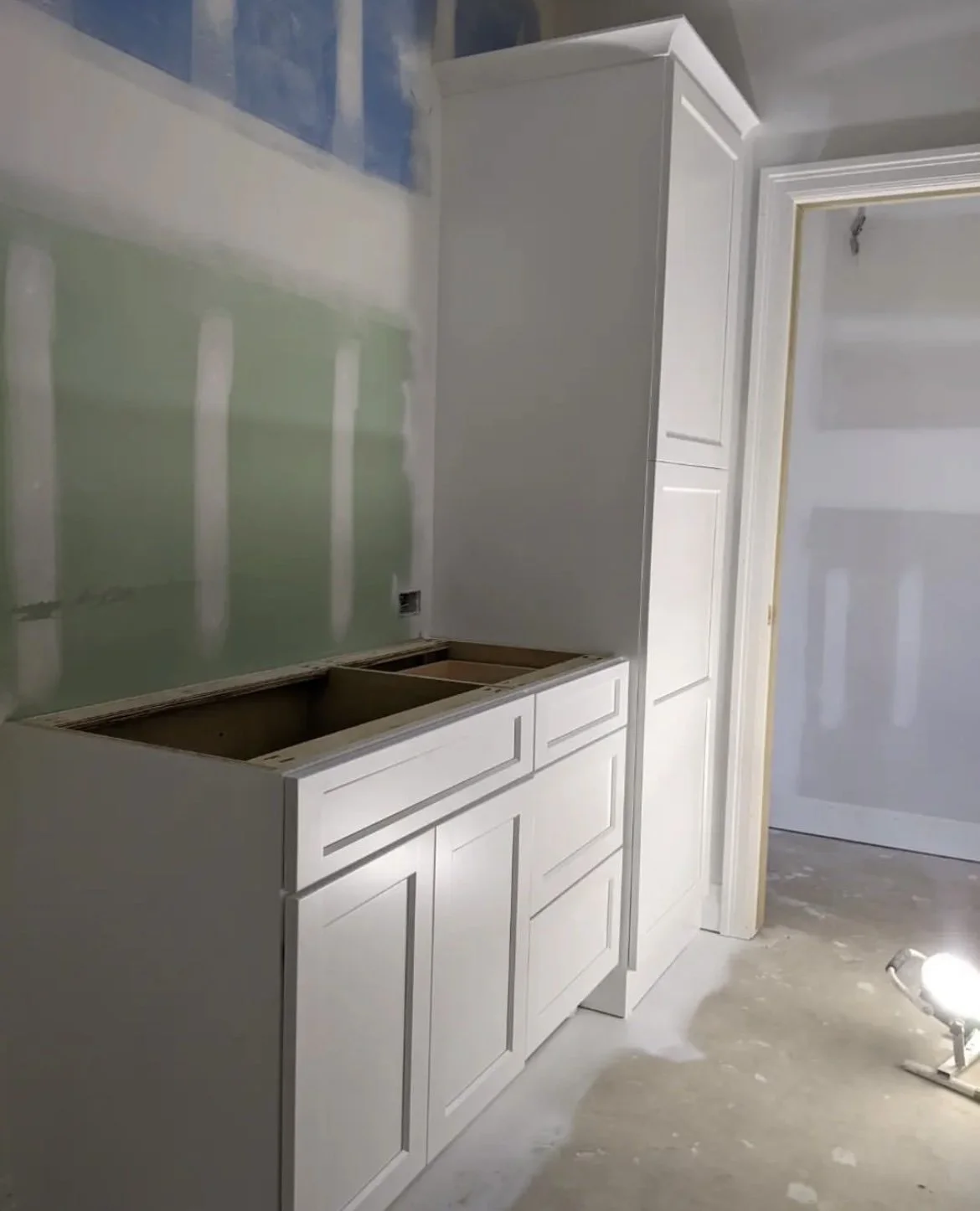 unfinished room with white cabinets installed, bare drywall, and construction lighting