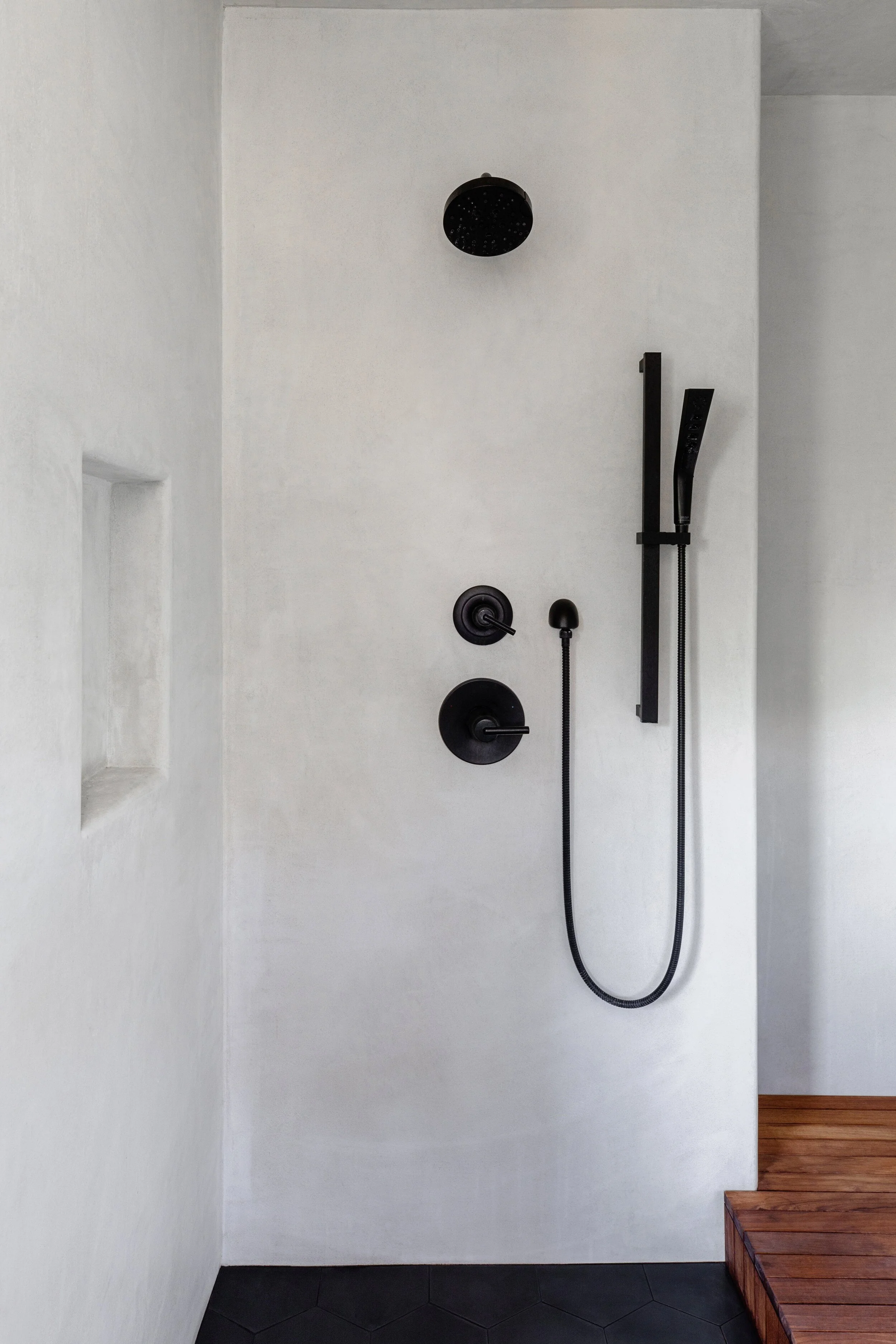Minimalist bathroom shower with black fixtures and step, white walls