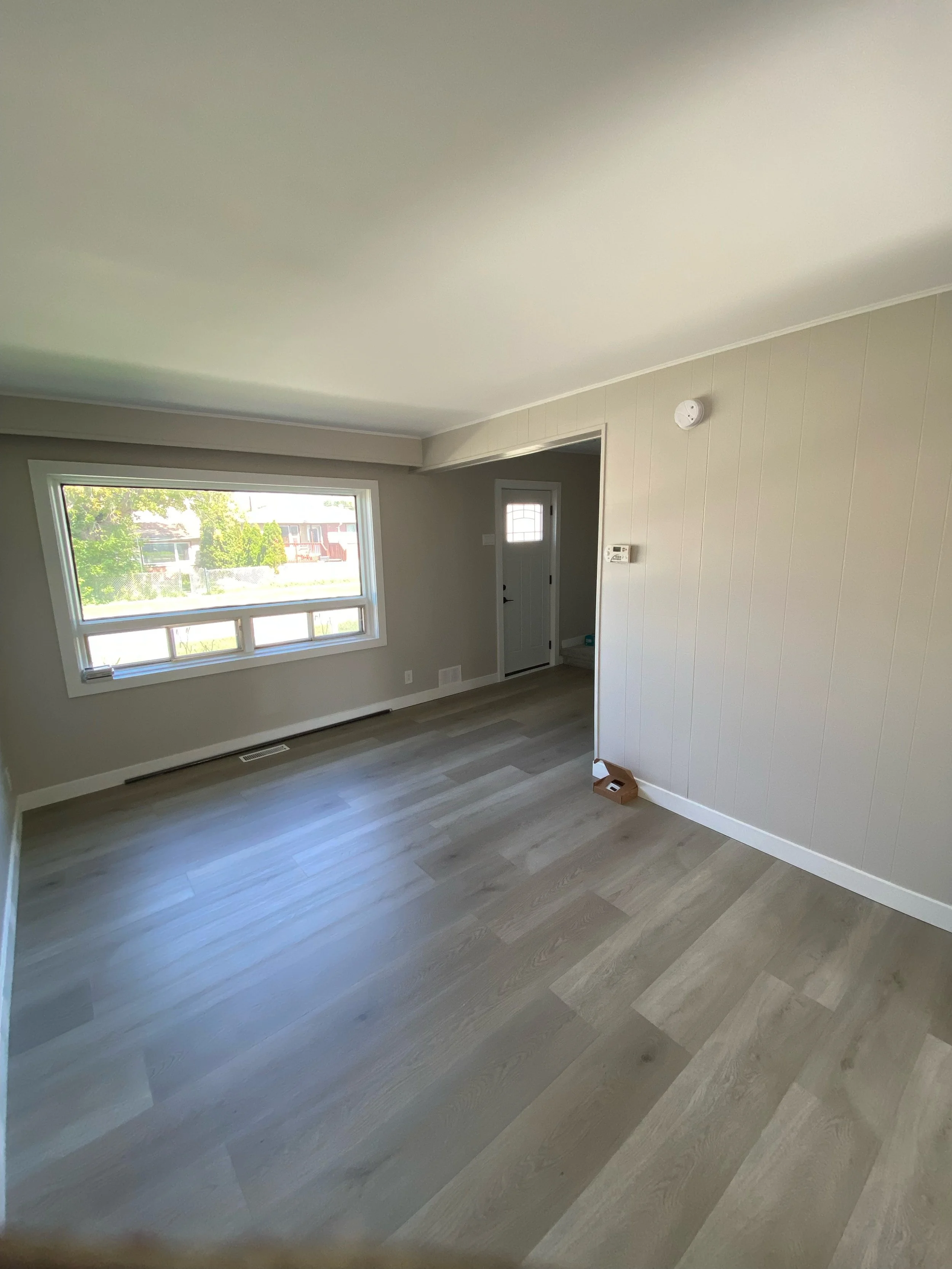 Empty room with light wood flooring, a large window, and a doorway.
