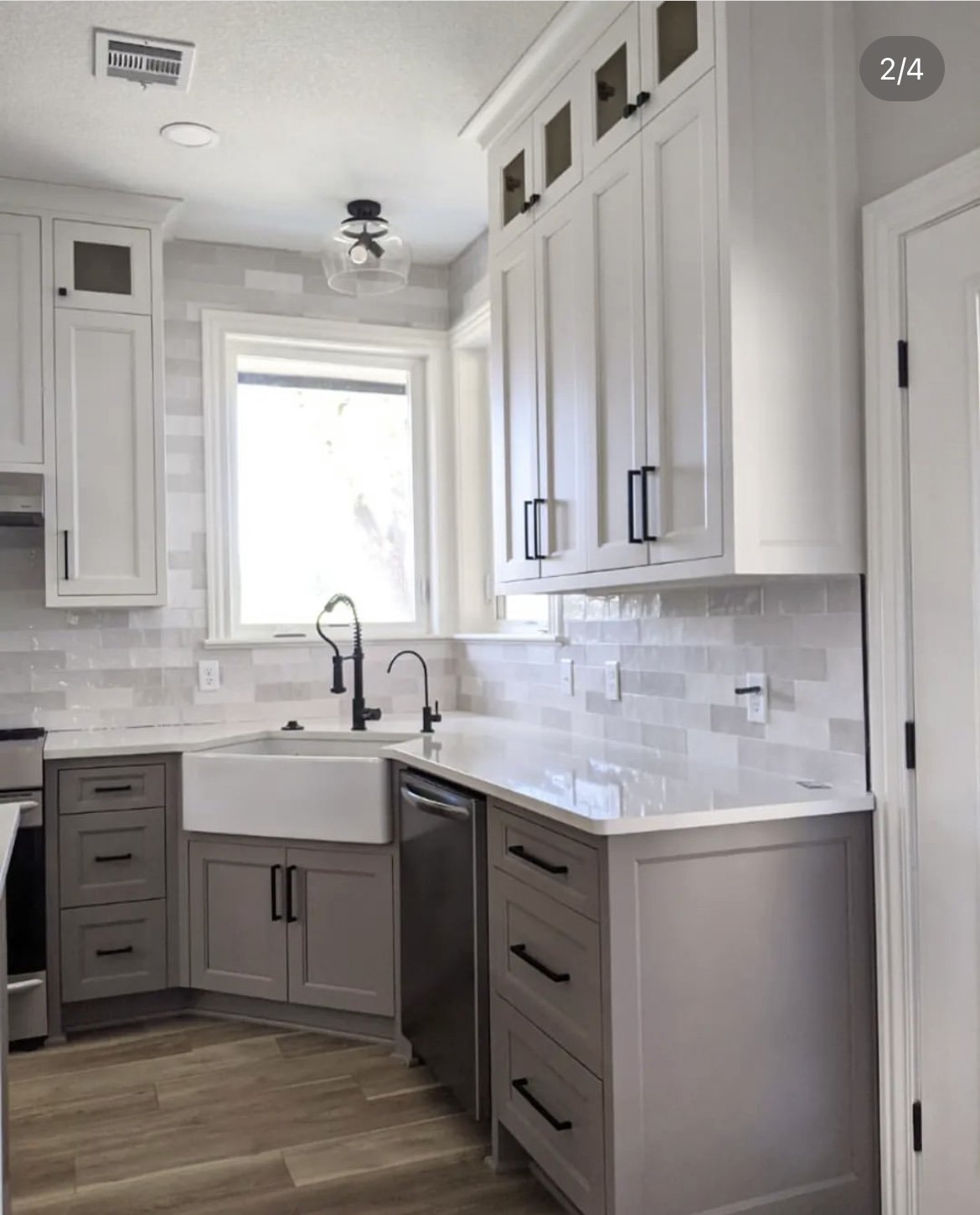 Modern kitchen with white cabinets, black handles, gray lower cabinets, a farmhouse sink with black faucet, stainless steel dishwasher, and white subway tile backsplash.