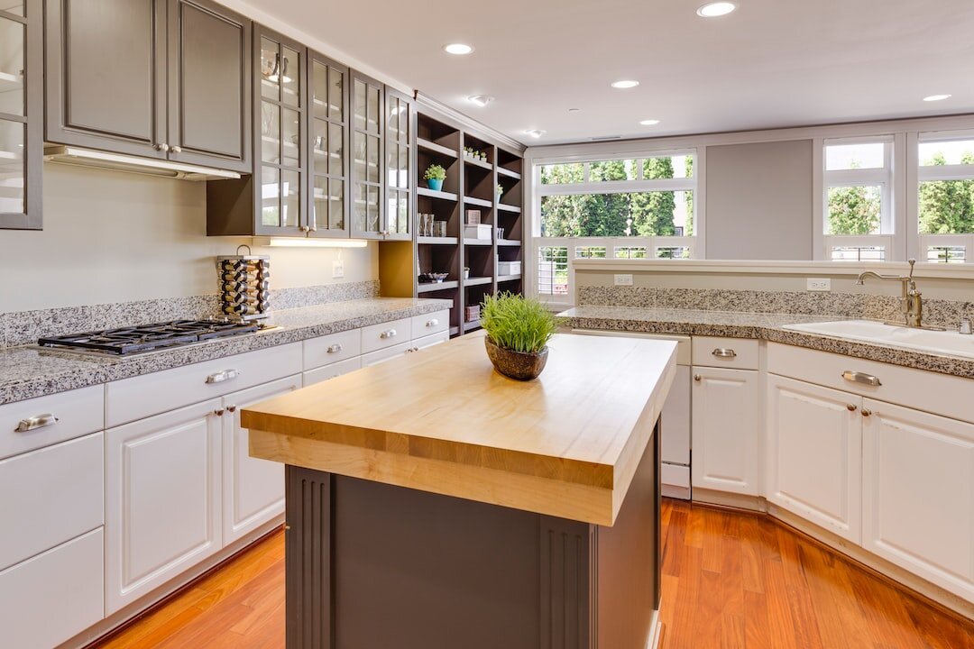 Modern kitchen with granite countertops, wooden island, white cabinets, glass cabinet doors, and greenery decor.