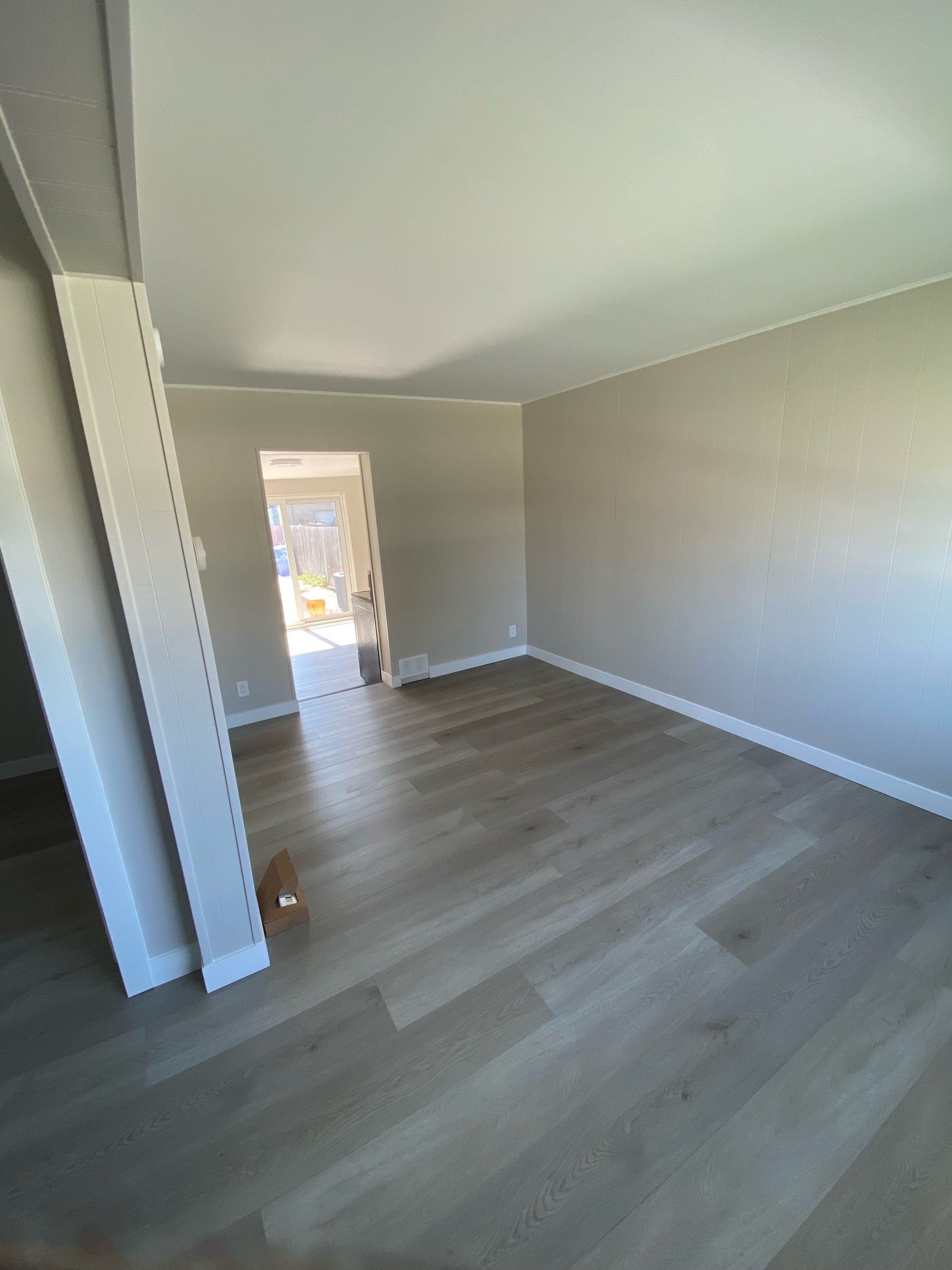 Empty room with light wood flooring and beige walls, featuring a doorway leading to a sunlit area.