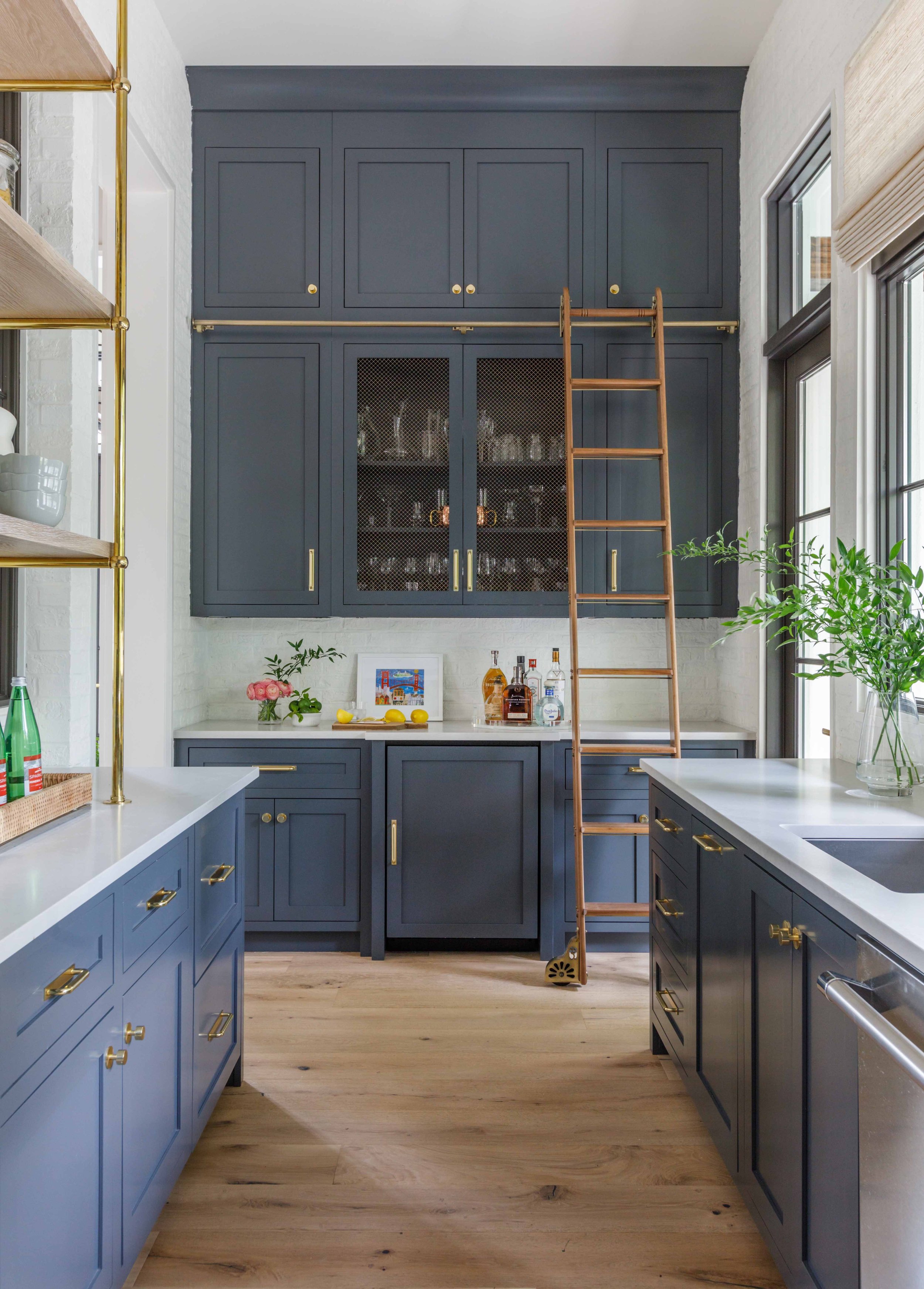 Modern kitchen with blue cabinets, brass hardware, and a wooden ladder.