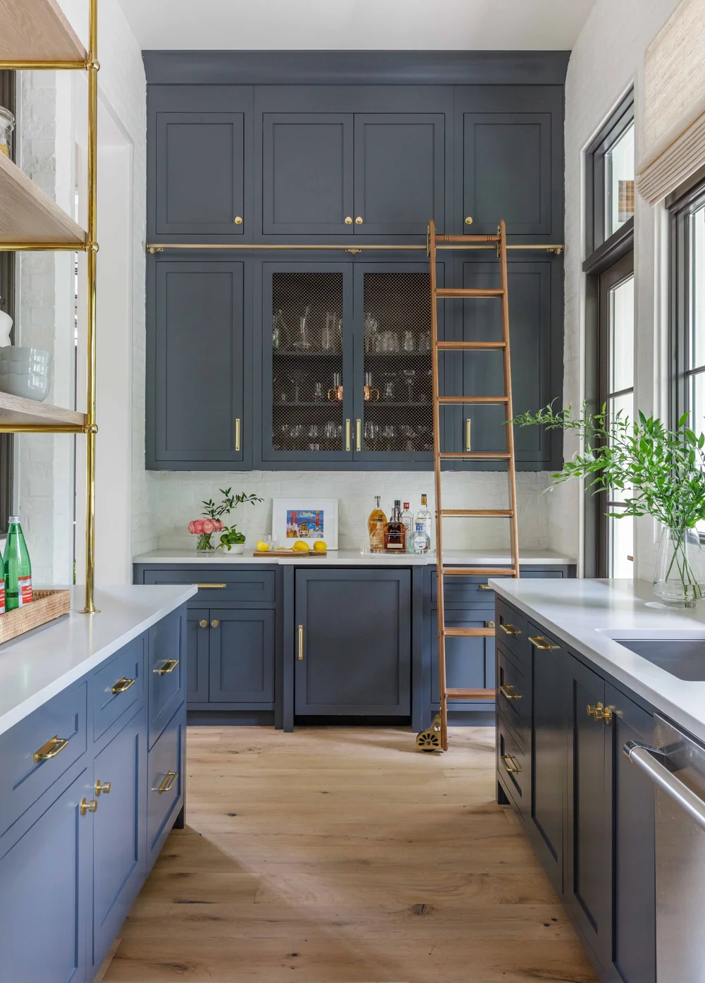 Blue kitchen cabinetry with brass hardware and a wooden ladder.