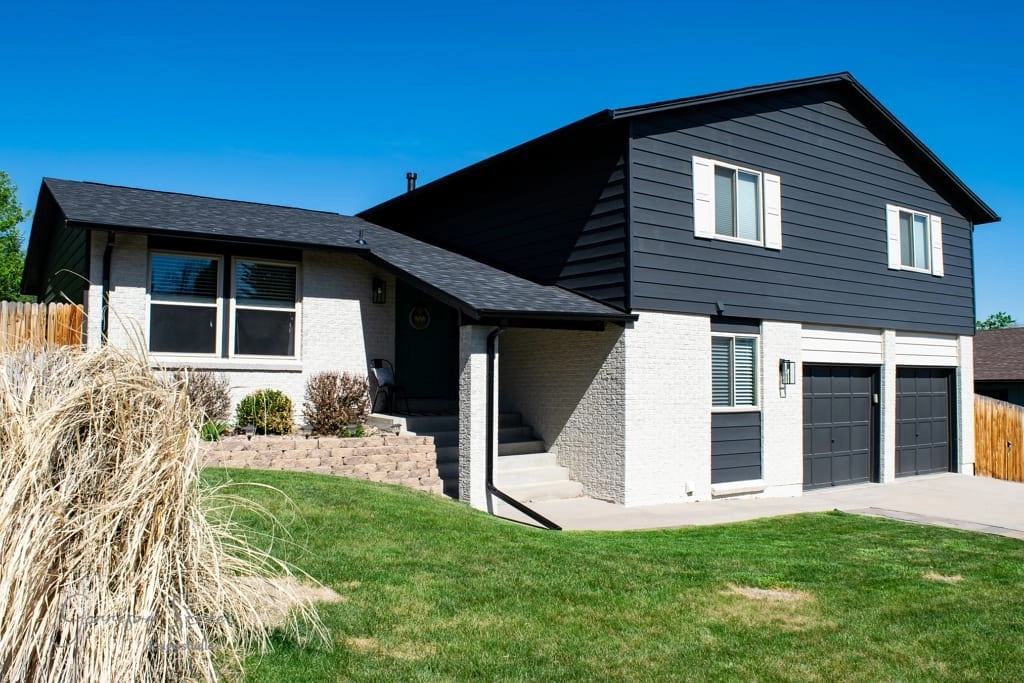 Modern two-story house with black and white exterior, two garages, and a front lawn with landscaping.