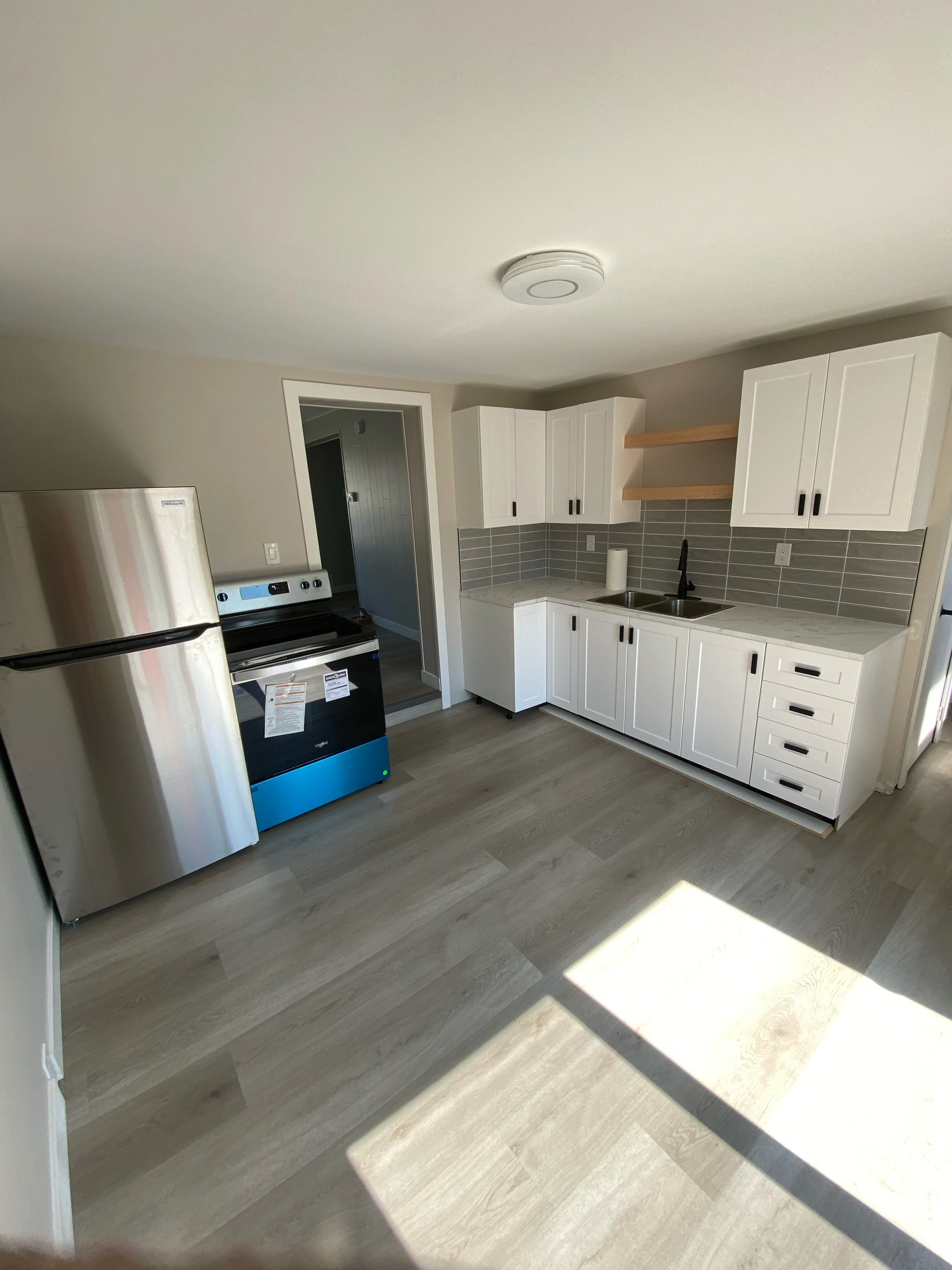 Modern kitchen with stainless steel appliances, white cabinets, light wood flooring, and tile backsplash.