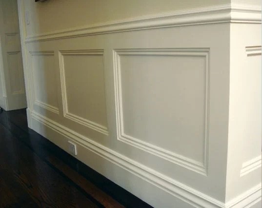 Wall with decorative wainscoting panels and dark wood floor.