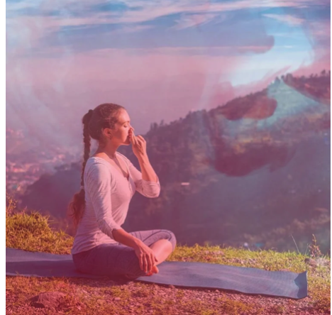 A woman practicing yoga outdoors on a mat, sitting in a cross-legged position with fingers near her nose, overlooking a scenic mountain view at sunrise or sunset.