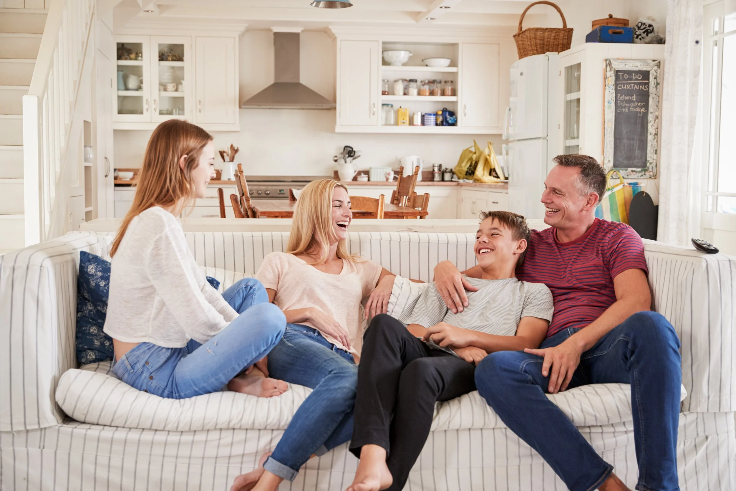 A family of four sitting on the living room couch talking and laughing.