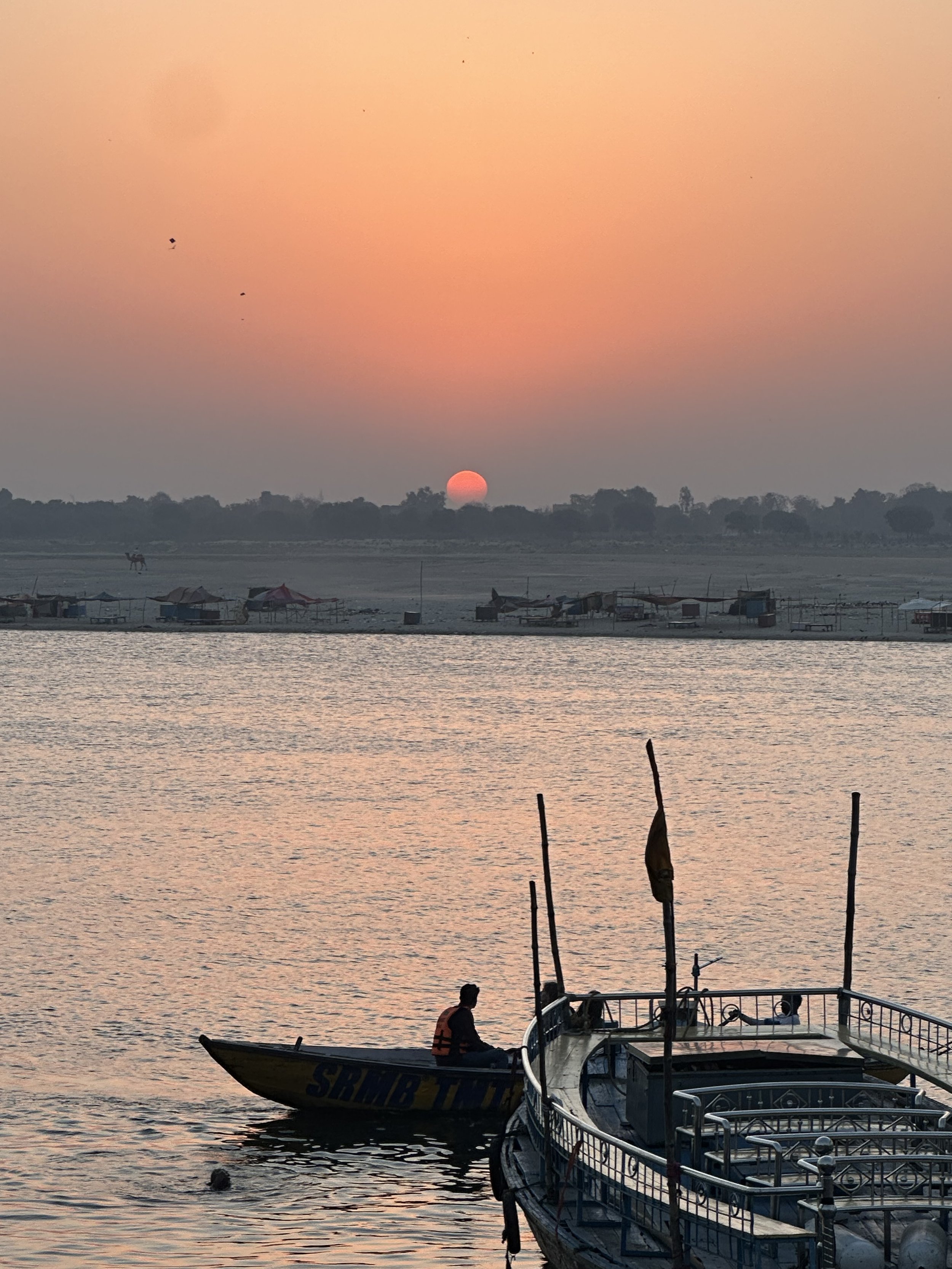Silhouette of a person on a boat at sunset, with calm water reflecting the orange sky.