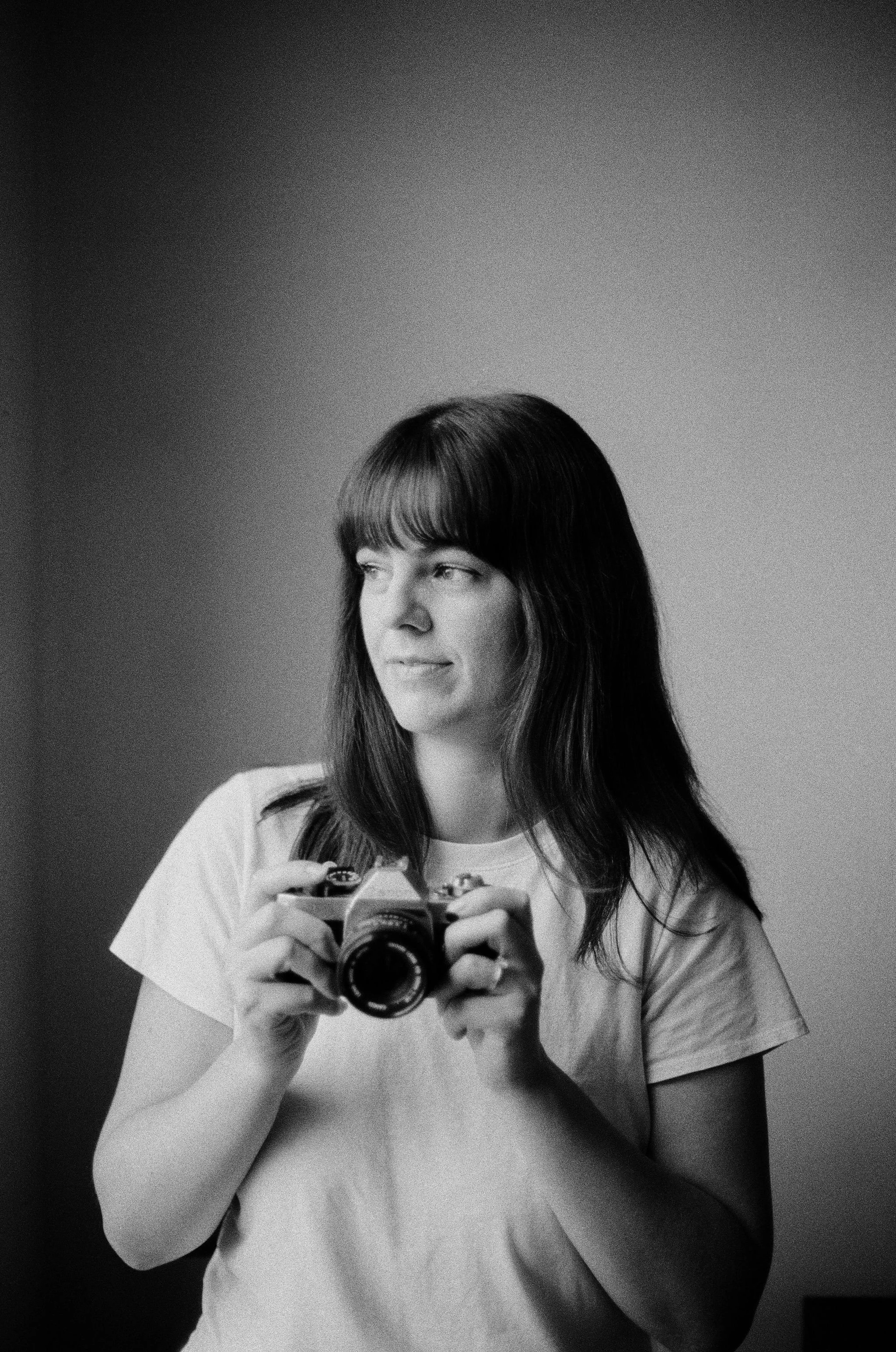 A photographer holding an old 35mm film camera and looking out a window.