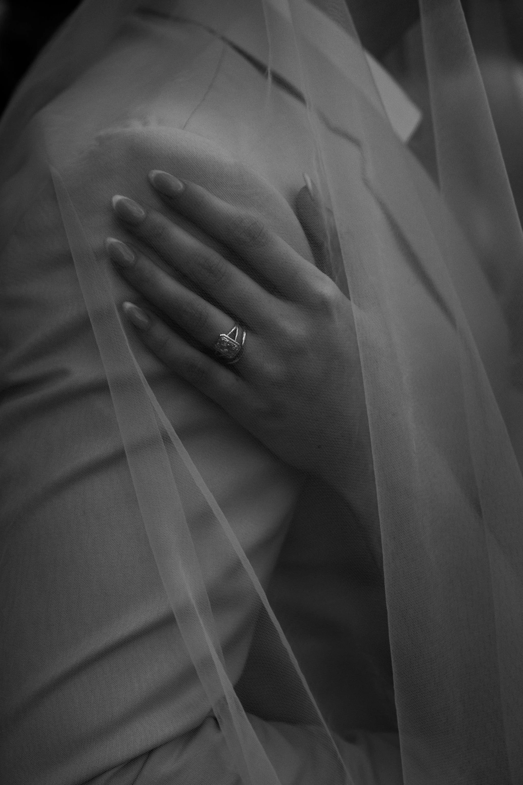 A bride places her manicured hand on her groom's shoulder, showing off her wedding ring.