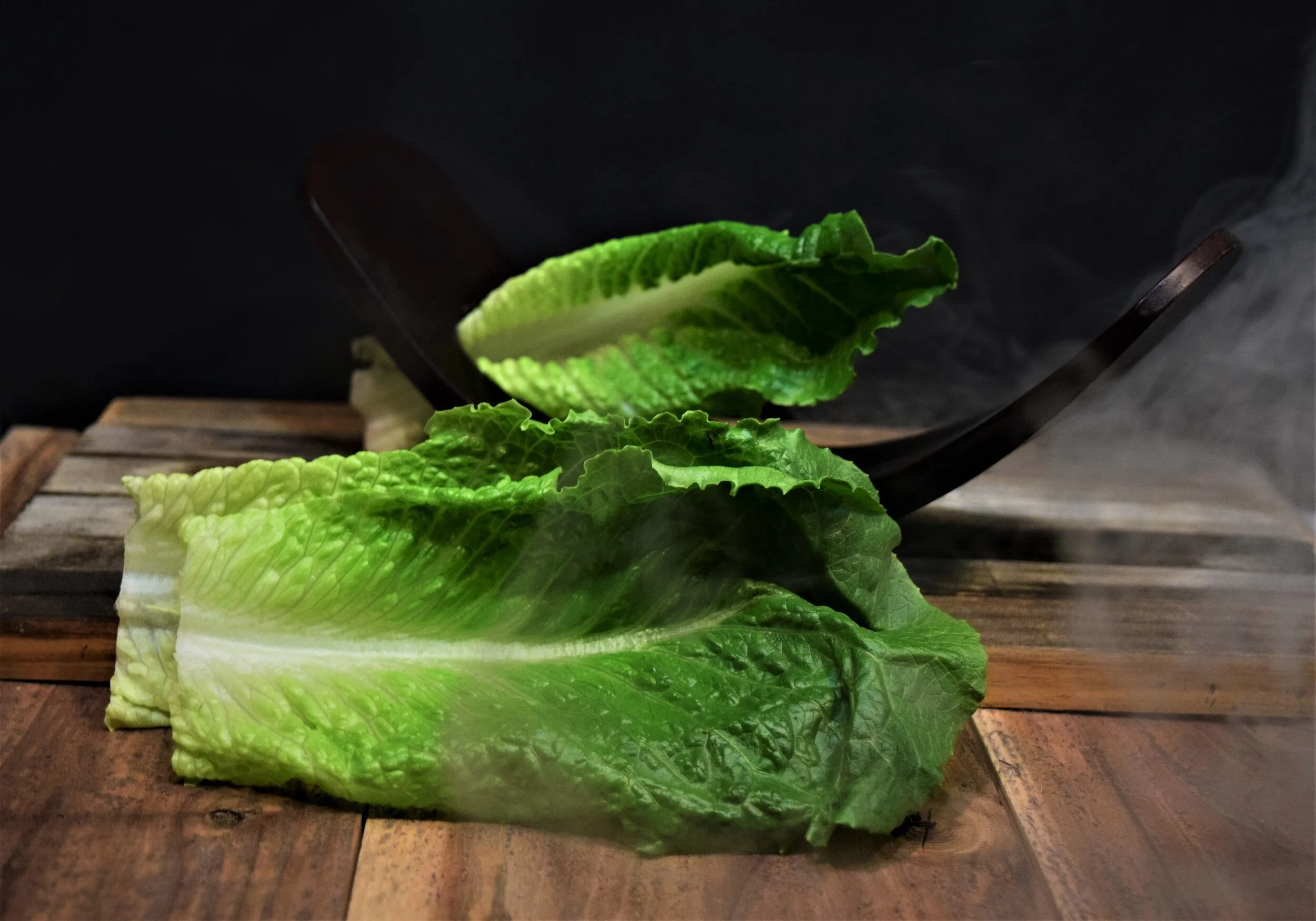 Fresh green lettuce leaves on a wooden surface with black background.