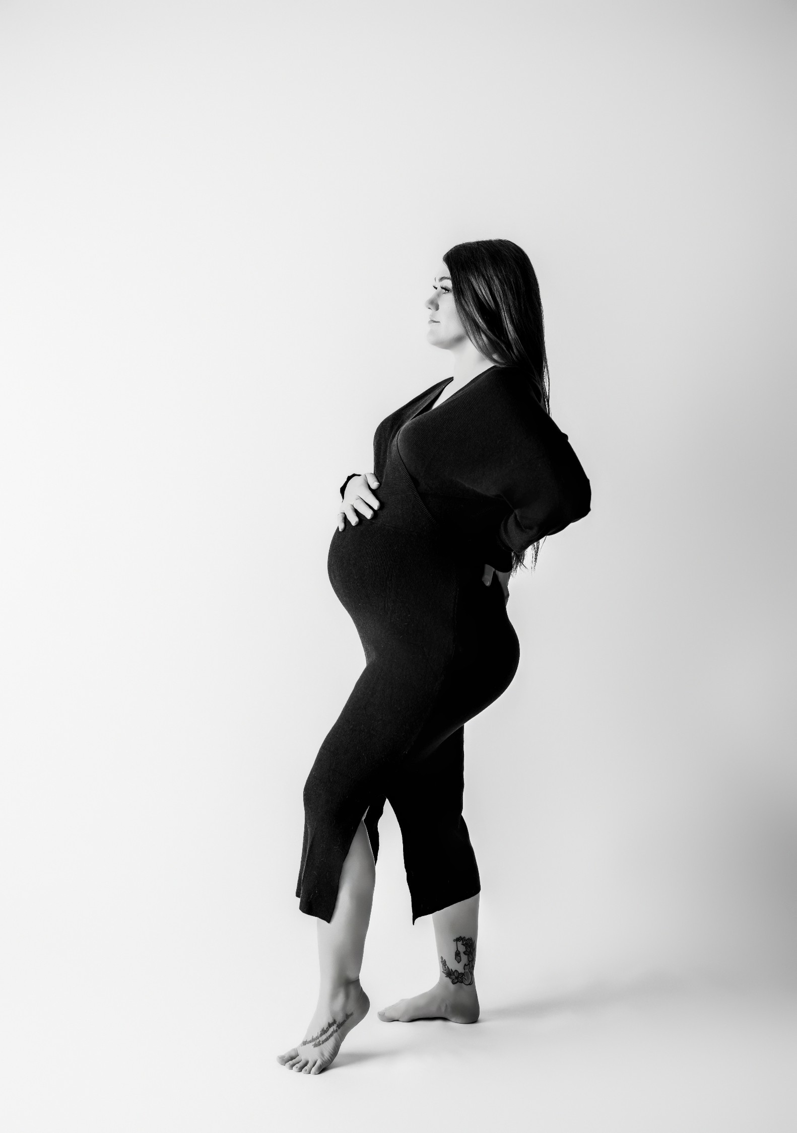 Silhouette-style black and white image of pregnant woman standing in profile during elegant studio maternity session
