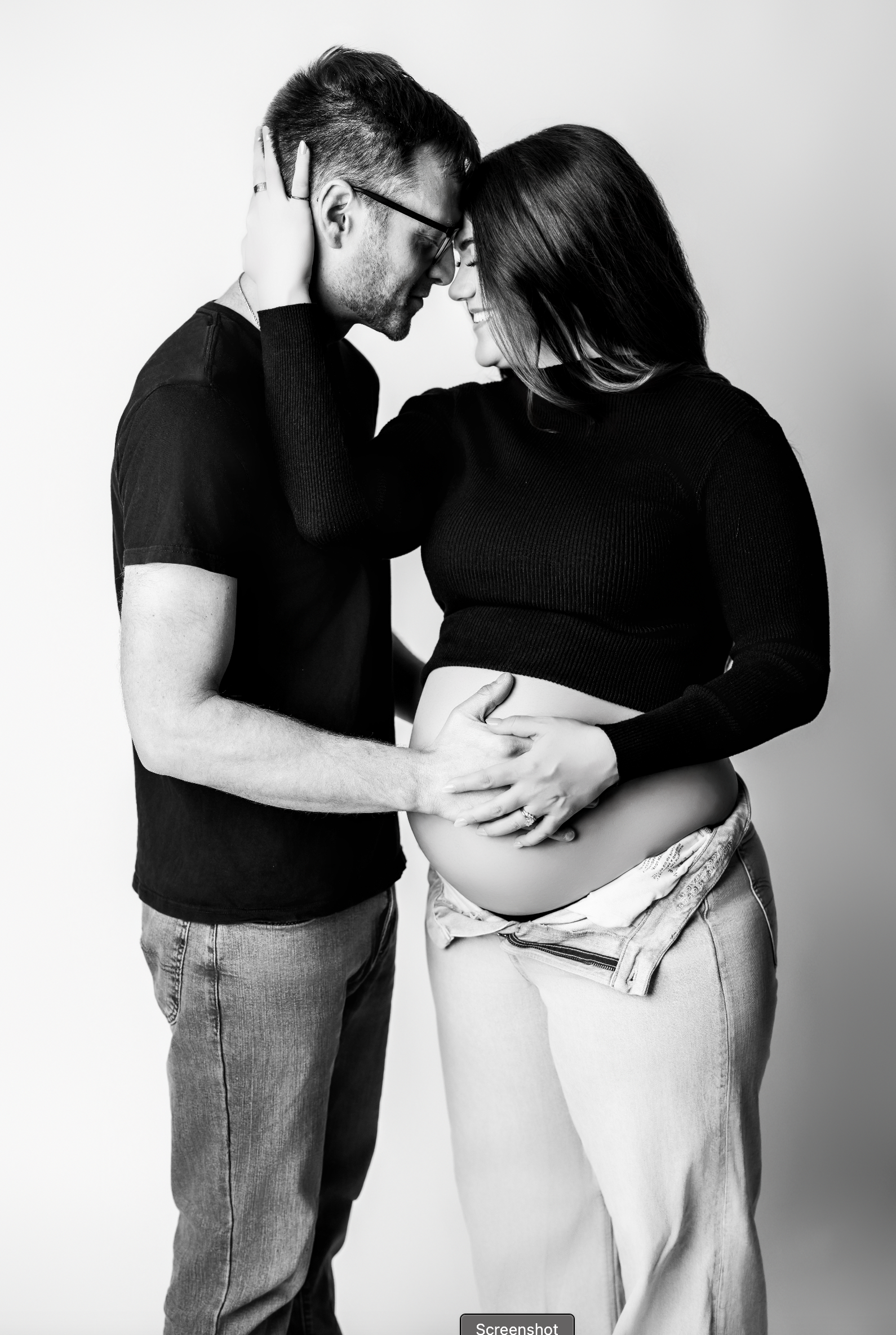 Close-up of couple embracing with hands on baby bump during intimate black and white maternity session