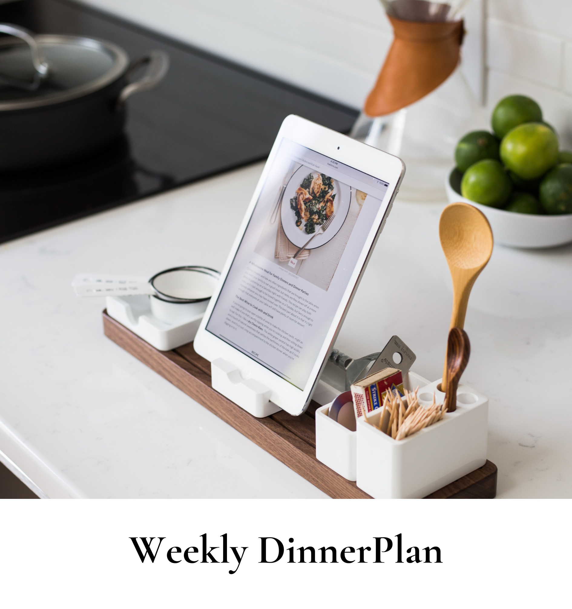 Tablet on a kitchen counter displaying a food photo and text, surrounded by a white condiment holder containing wooden spoons, stir sticks, and condiments, with a bowl of limes and a copper pitcher nearby.