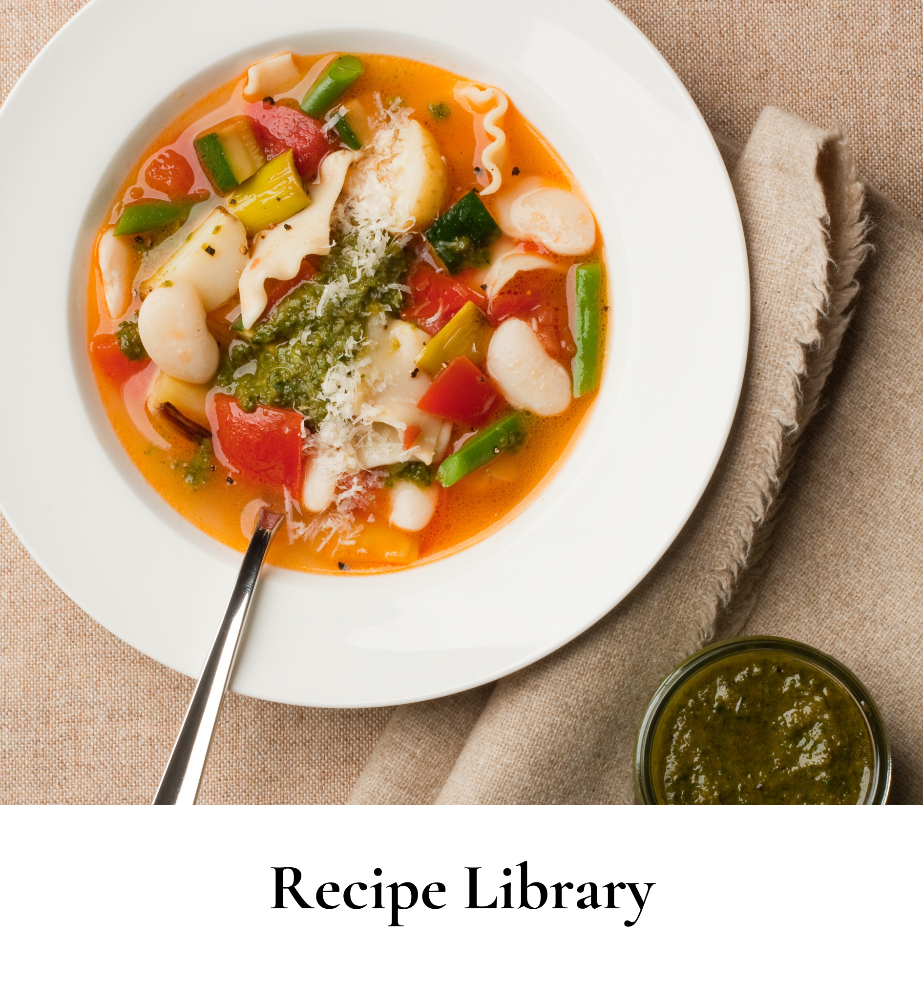 Bowl of vegetable minestrone soup with colorful vegetables and grated cheese, served with a side of pesto sauce.