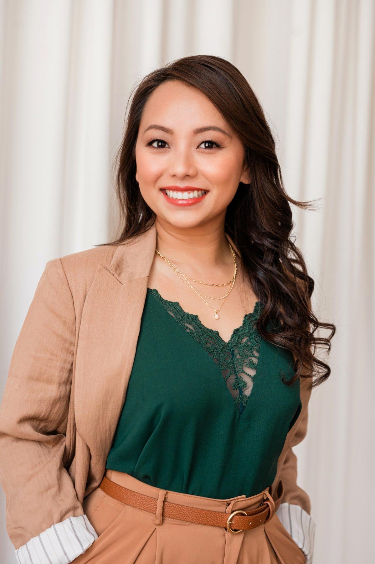 Karissa smiles green blouse tan jacket against white drapey background