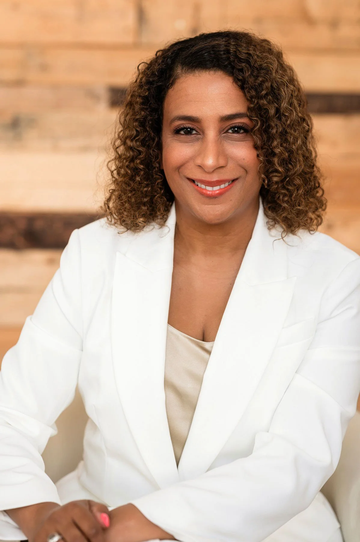 Alison Battiste Clement smiles white suit against wooden wall background