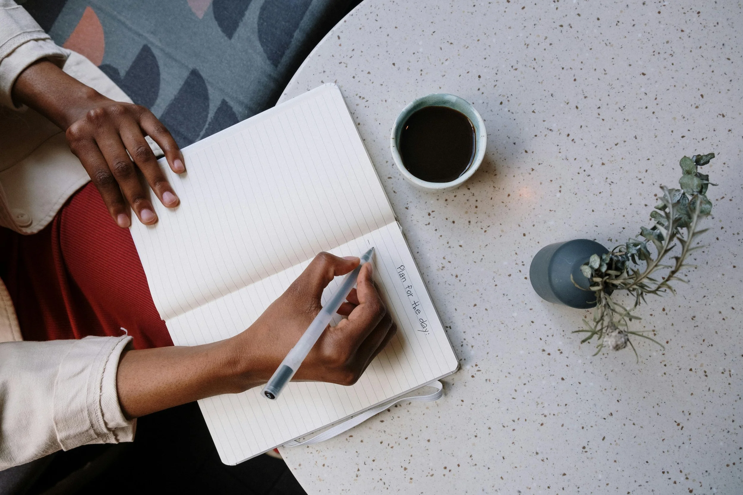 Overhead view of person writing in lined journal with coffee cup