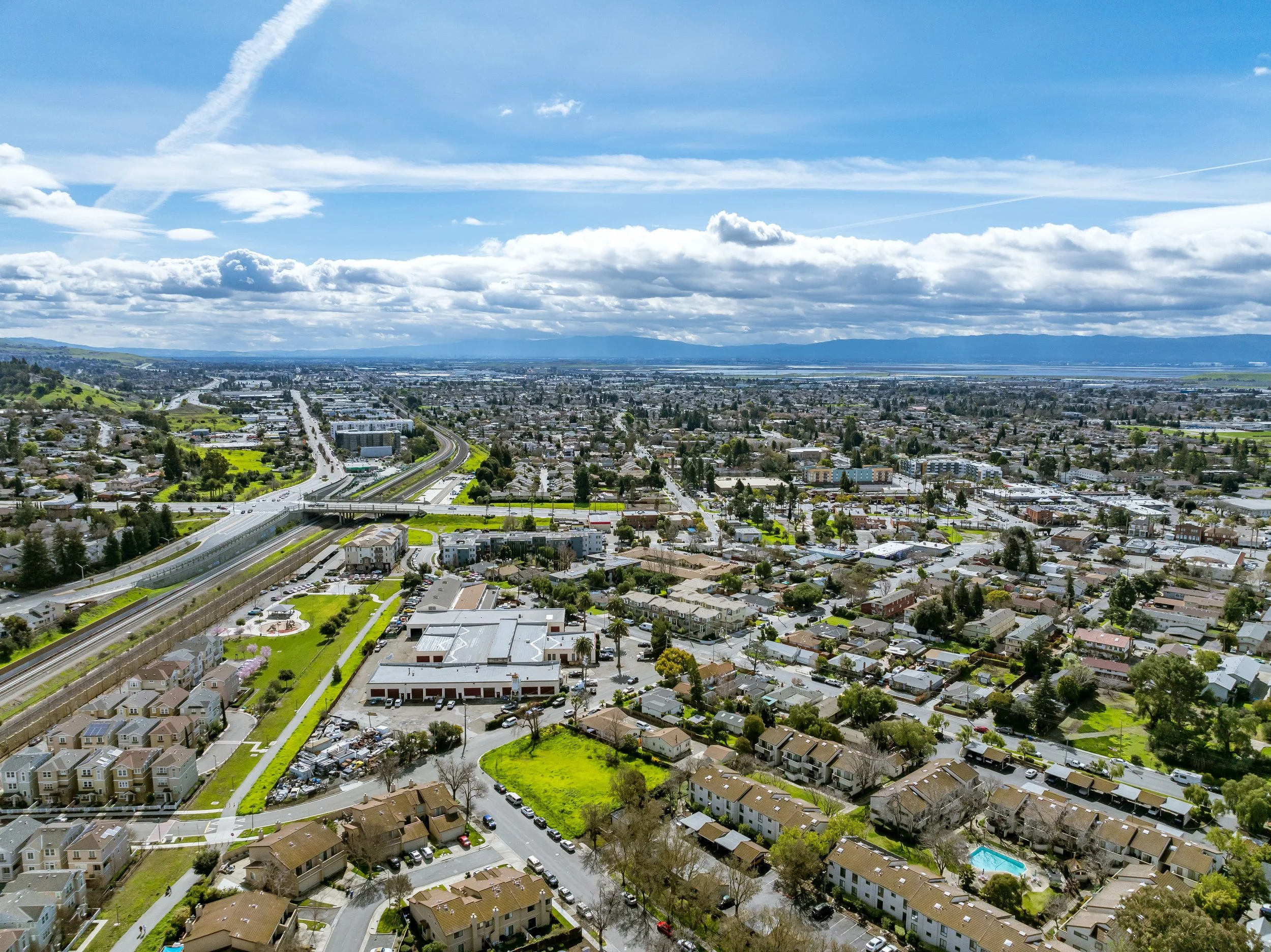 Aerial view of a city with residential houses, commercial buildings, a highway, and green areas under a partly cloudy sky. Minneapolis, Minnesota