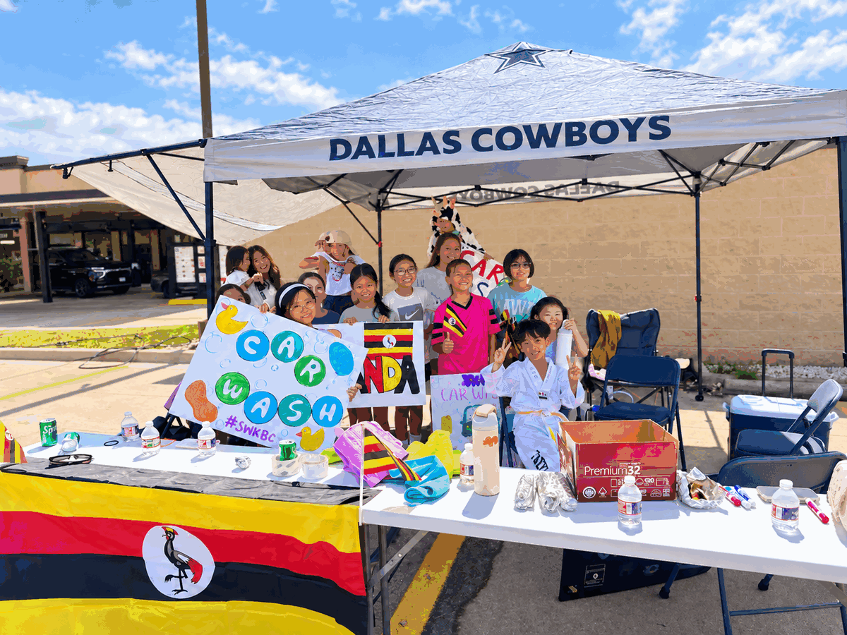 Southwestern Korean Baptist Church volunteers gather with car wash signs and a Uganda flag at the fundraiser.