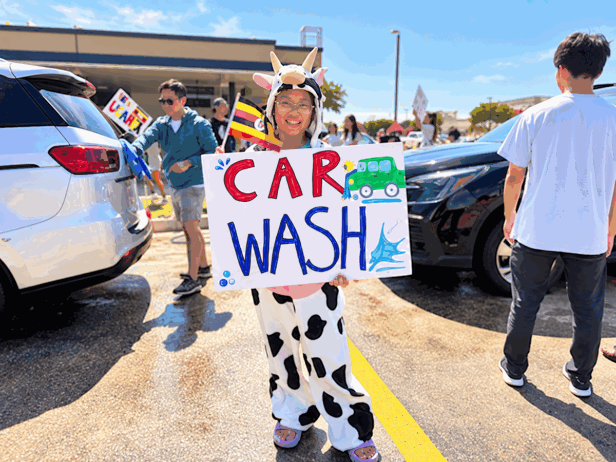 A volunteer in a cow costume holds a handmade car wash sign at the Uganda fundraiser.