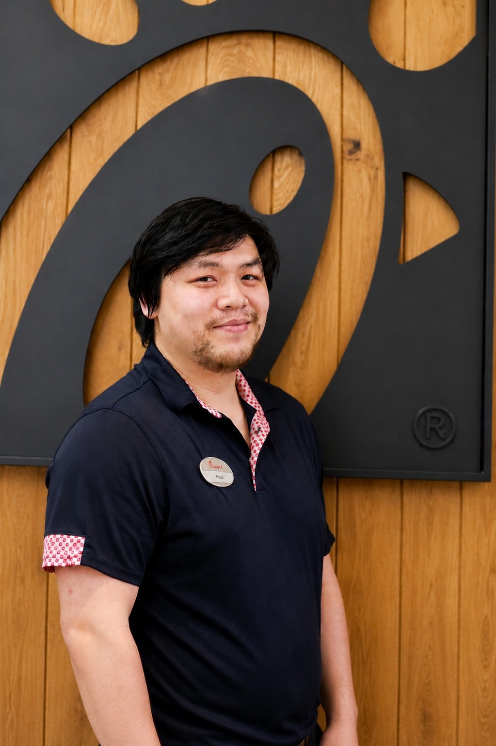 Phai Nguyen smiling in front of the Chick-fil-A logo wall inside the restauran