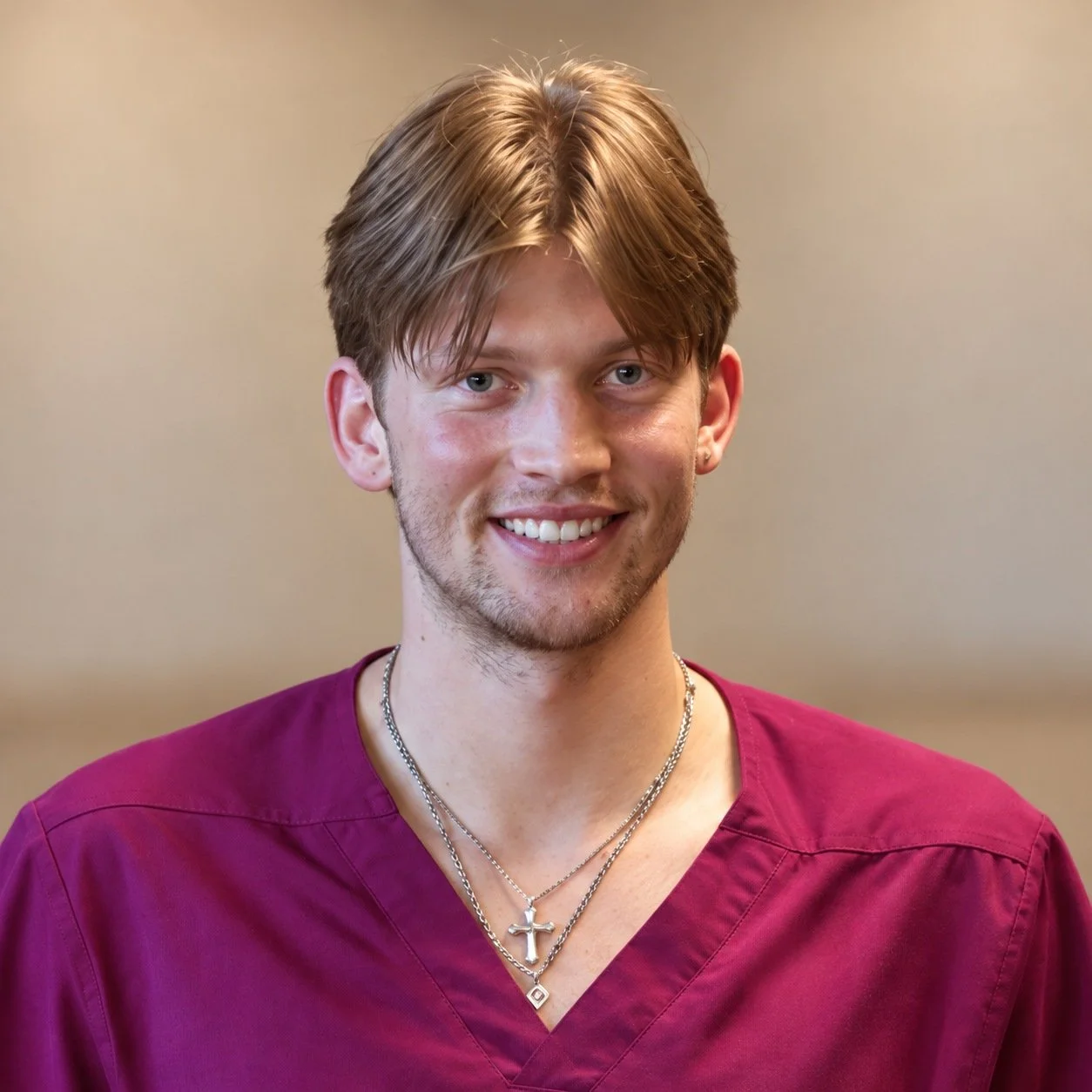 Evan Olson smiling in maroon scrubs against a softly blurred neutral background.