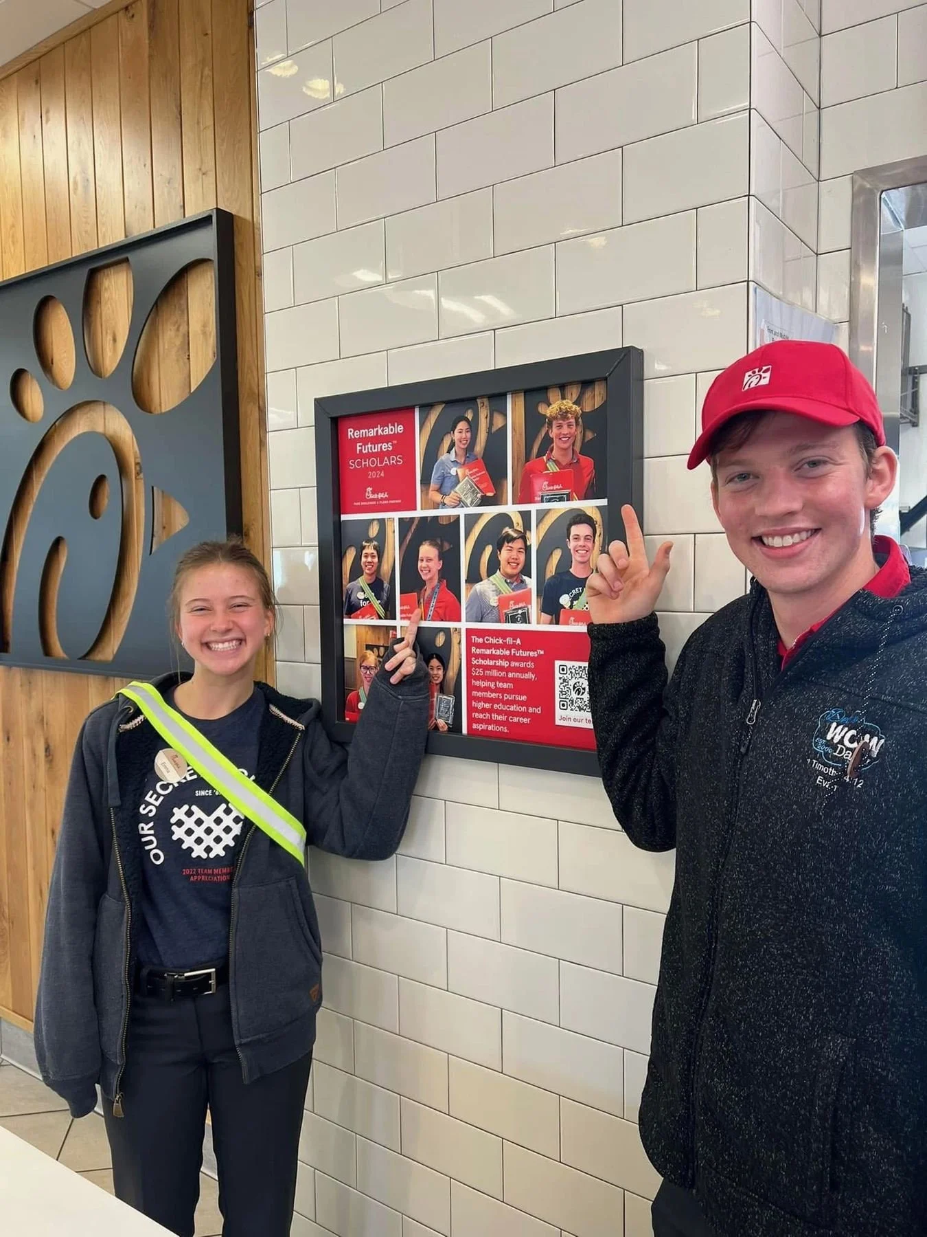 Evan Olson and a coworker pointing to the Remarkable Futures Scholars display at Chick-fil-A Park.
