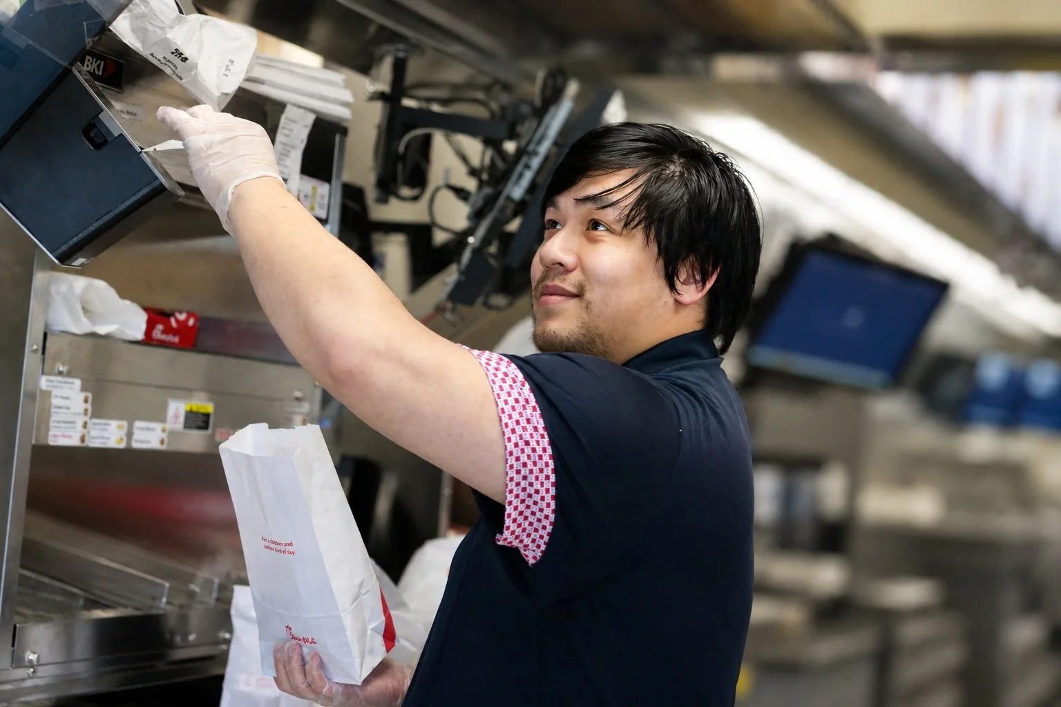 Phai Nguyen reaching for order tickets at the kitchen rail during a busy shift at Chick-fil-A Park Blvd. in Plano, Texas