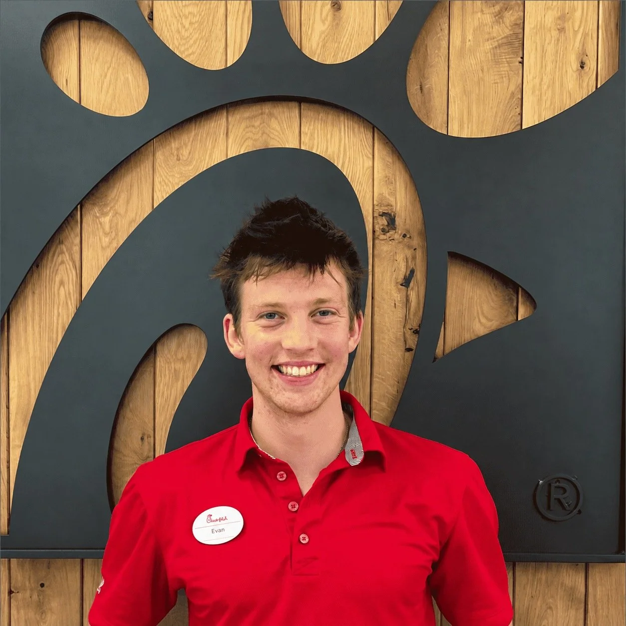 Evan Olson smiling in his red Chick-fil-A uniform in front of the restaurant logo