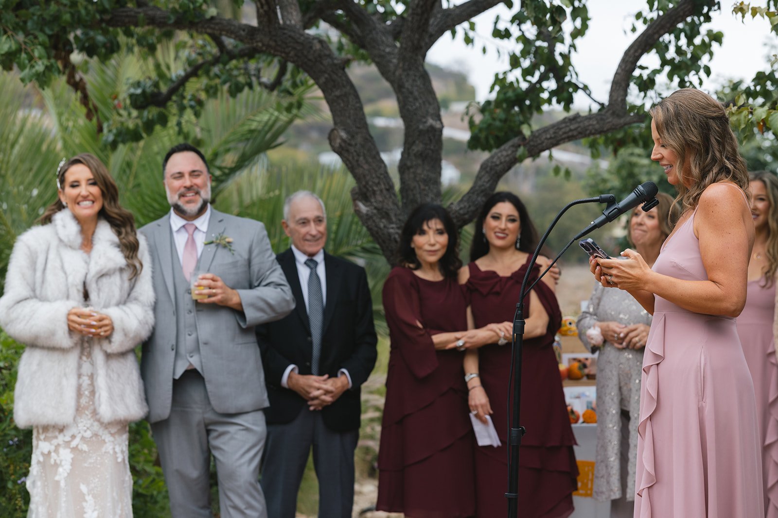 Bride and groom Zack and Kimberly listen to heartfelt maid of honor speeches during their outdoor Malibu wedding reception, surrounded by family and friends at a private estate.