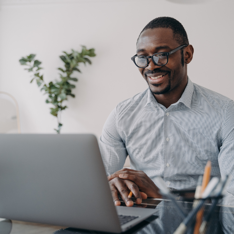 A man with glasses working on a laptop in a modern office.
