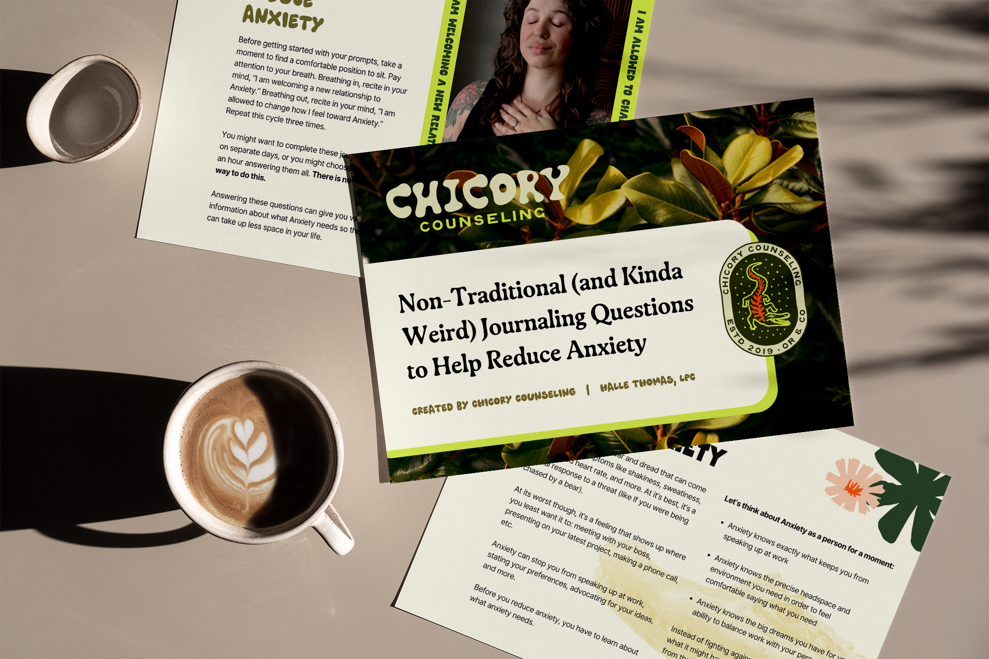 A table with two coffee cups and three pamphlets or worksheets about anxiety and journaling, one labeled "Chicory Counseling" with a green and brown leaf design, another titled "Non-Traditional (and Kinda Weird) Journaling Questions to Help Reduce Anxiety," and a third partially visible with green and pink floral designs. One coffee cup has latte art in the shape of a heart.