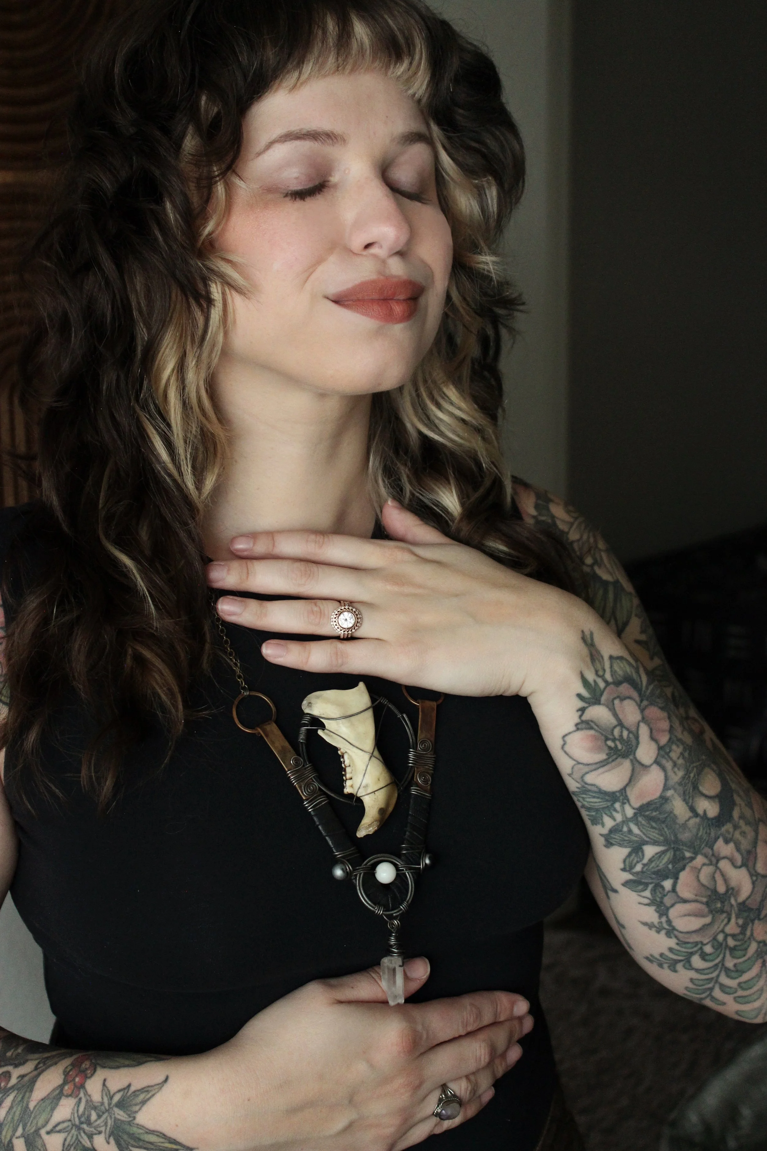 Halle Thomas, a BIPOC anxiety therapist serving high achievers in Portland, Oregon. She is a pers with curly hair and tattoos on her arms, eyes closed, smiling gently, wearing a ring and a necklace with a large pendant, holding her hand to her chest.