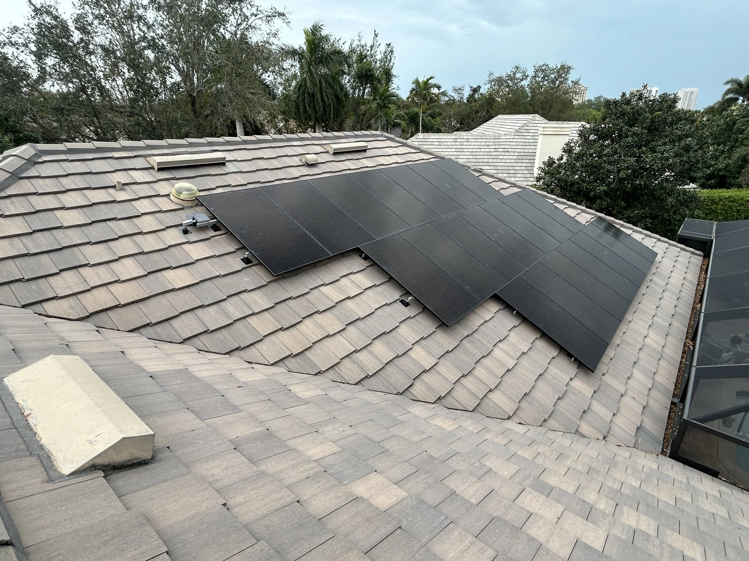 Residential roof with solar panels installed, surrounded by trees and neighboring houses.