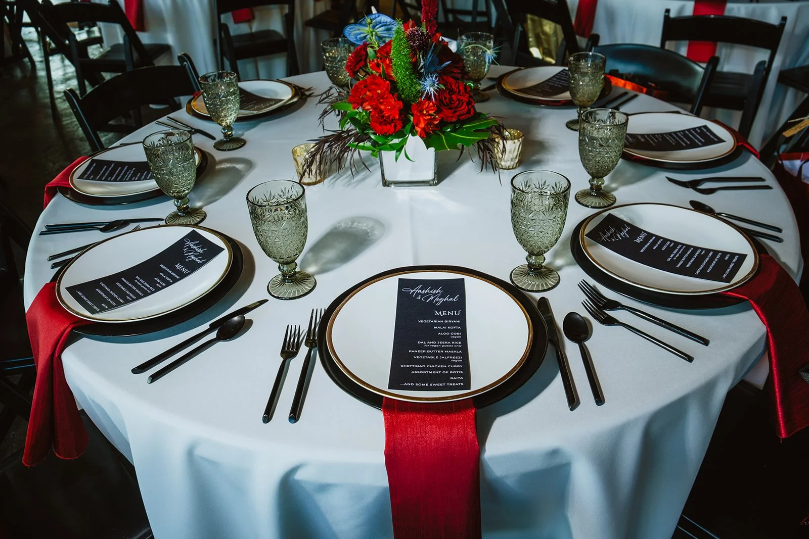 A round table set for a formal event with black accents, a colorful flower centerpiece, and black and red accents on the tablecloth and napkins.