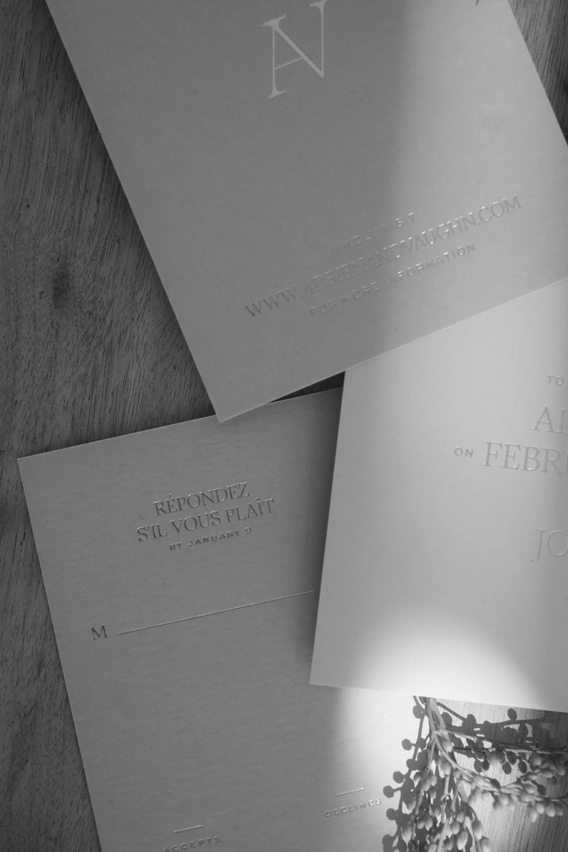 Three printed cards with embossed text, placed on a wooden surface with a sprig of small round leaves. The cards contain French text and website information.
