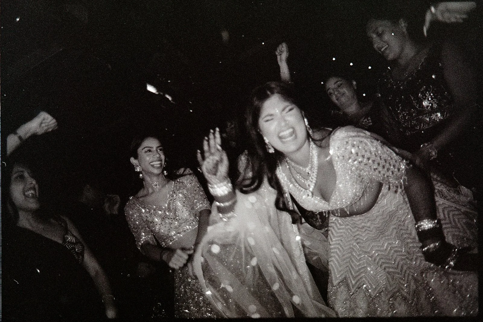 Group of women dancing and celebrating at a party, dressed in traditional Indian attire, smiling and enjoying themselves.